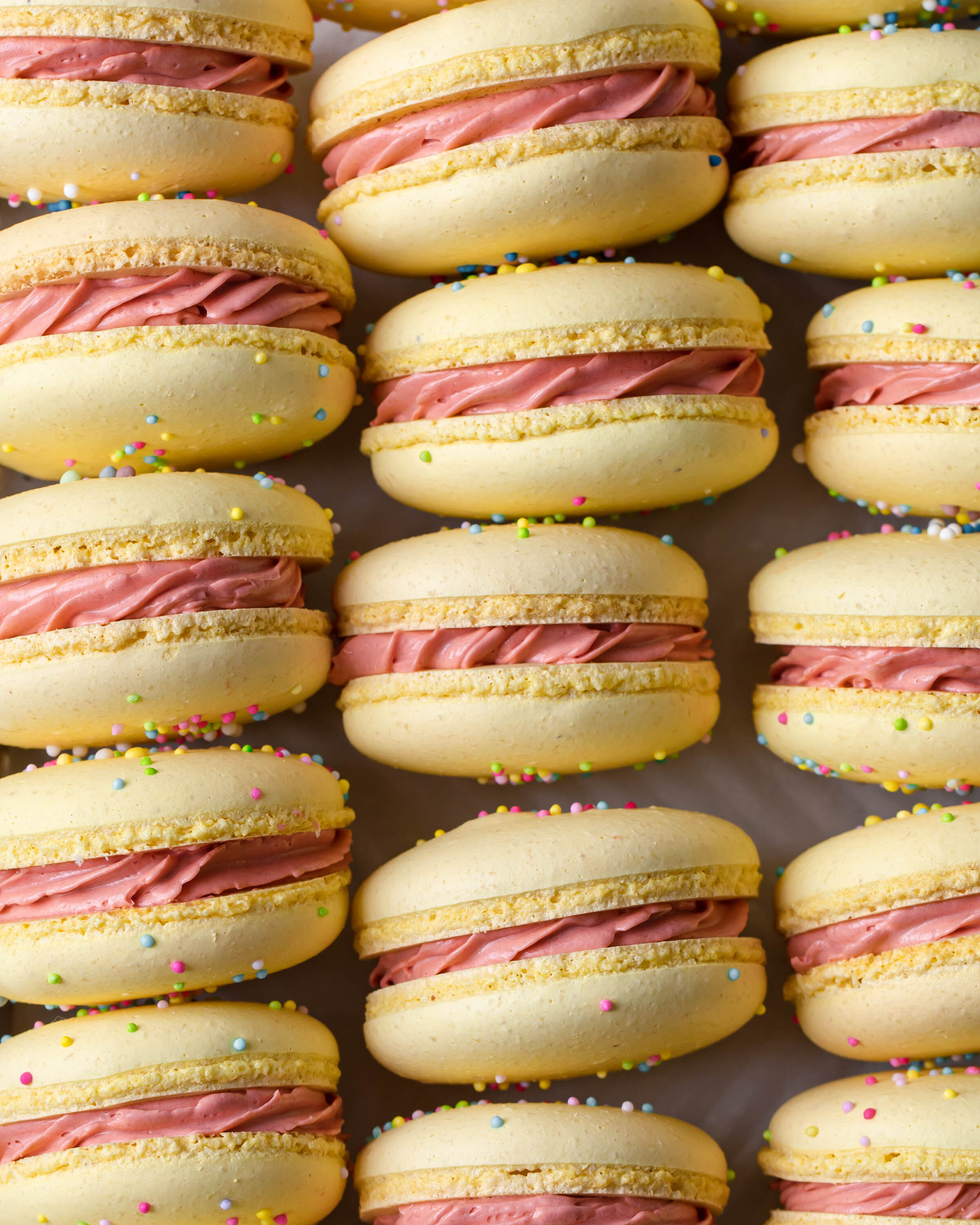 A close-up picture of yellow French macarons with sprinkles and pink buttercream filling