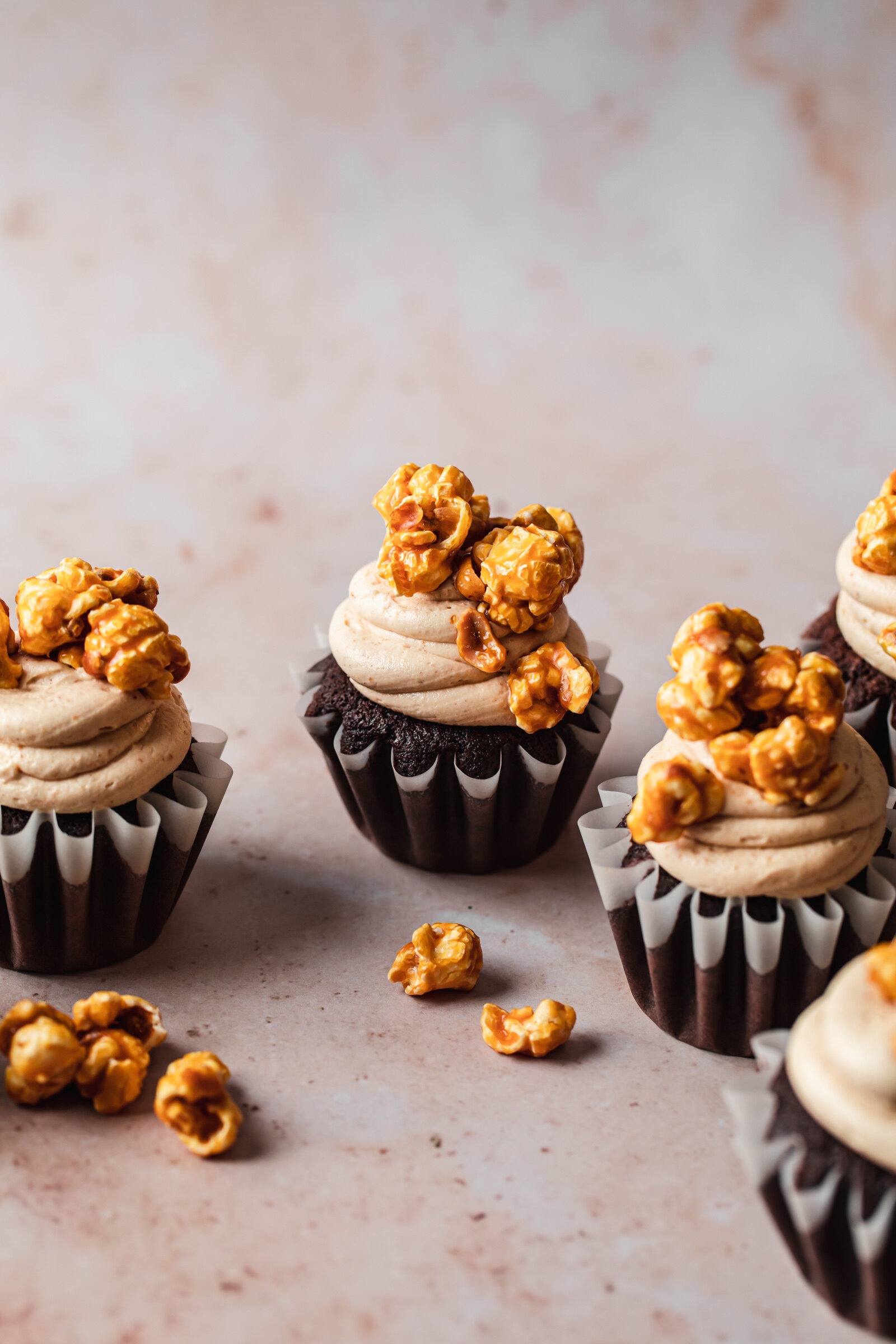Chocolate cupcakes on a beige marble table with creamy peanut butter frosting and caramel popcorn on top.