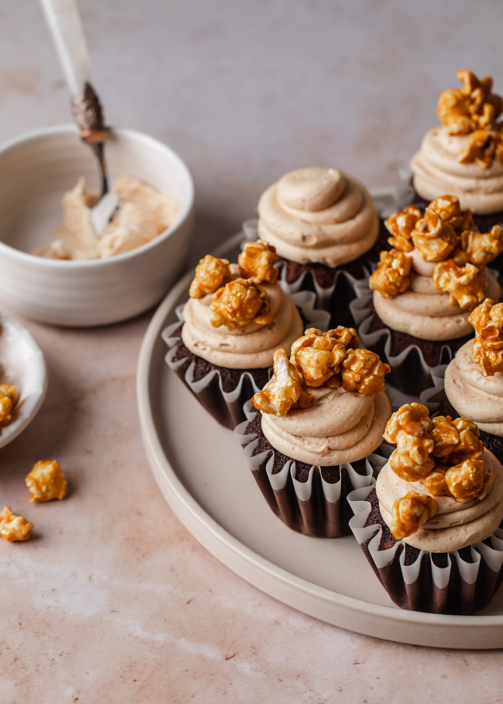 A serving plate of chocolate cupcakes  with creamy peanut butter frosting and caramel popcorn on top.