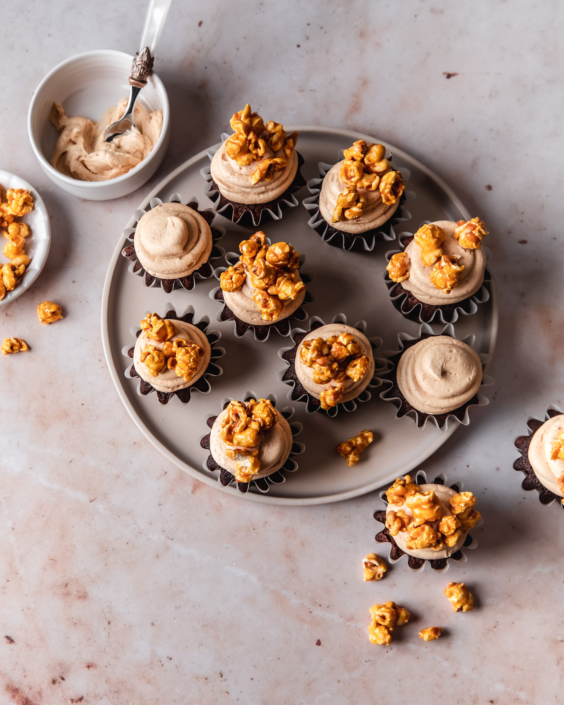 An overhead shot of a  serving plate of chocolate cupcakes with creamy peanut butter frosting and caramel popcorn on top.