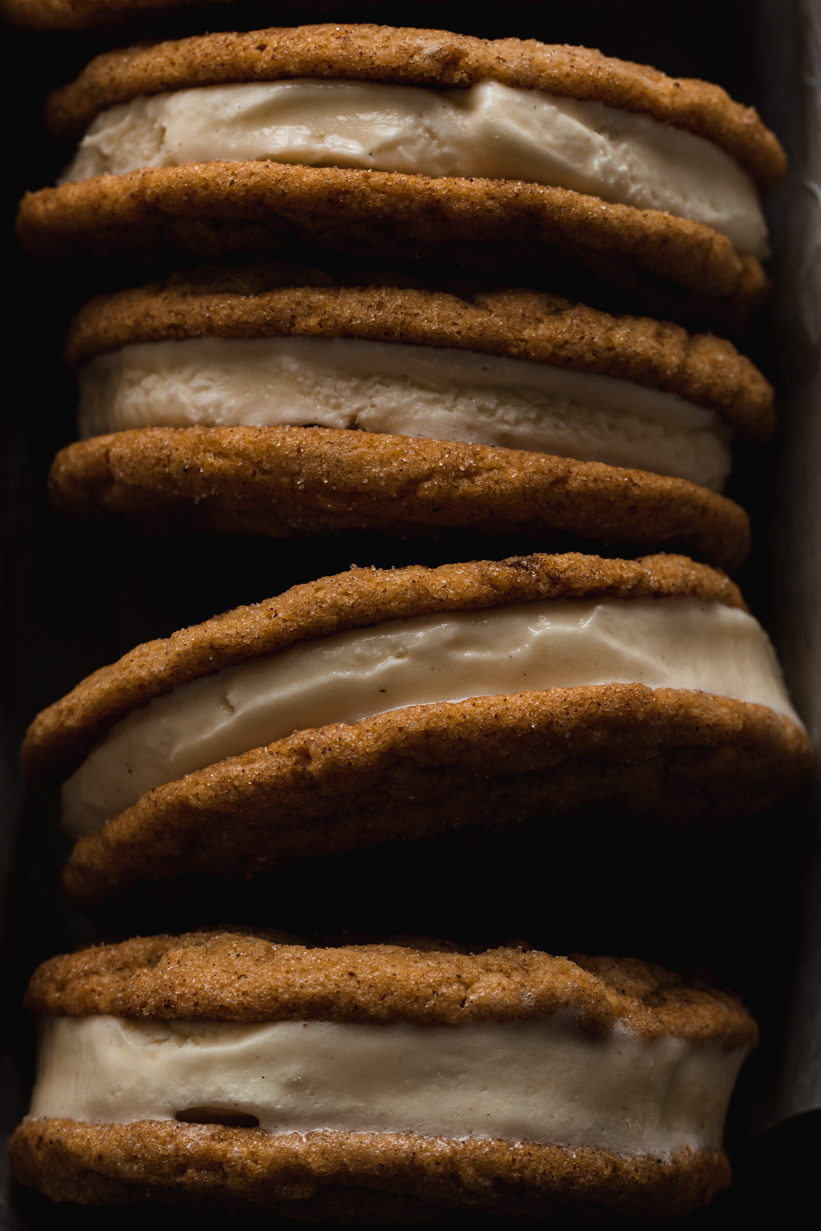 A dark and moody photo of Pumpkin Snickerdoodle Ice Cream Sandwiches stacked on thier sides.