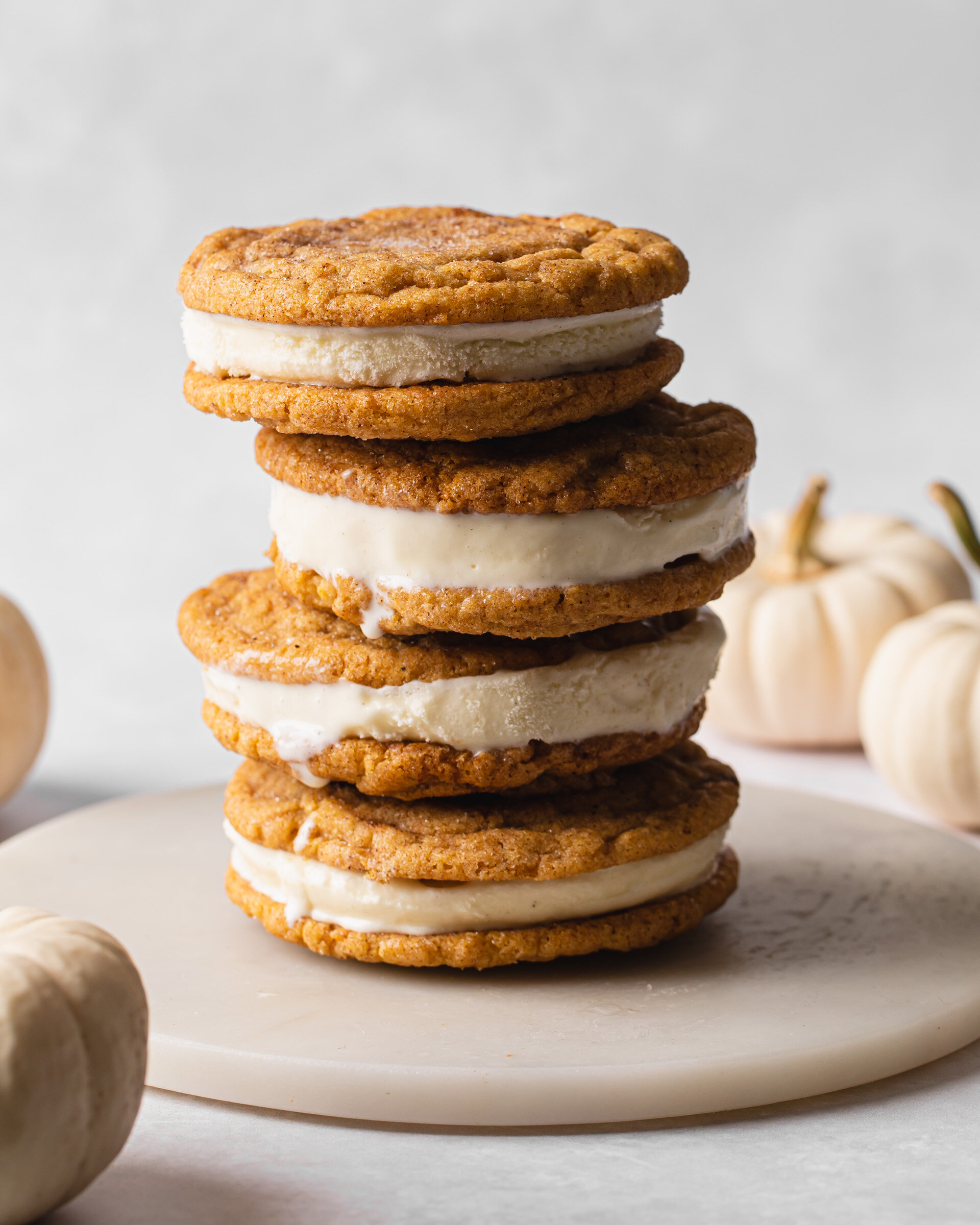 Pumpkin Snickerdoodle Ice Cream Sandwiches stacked vertically with mini white pumpkins in the background.
