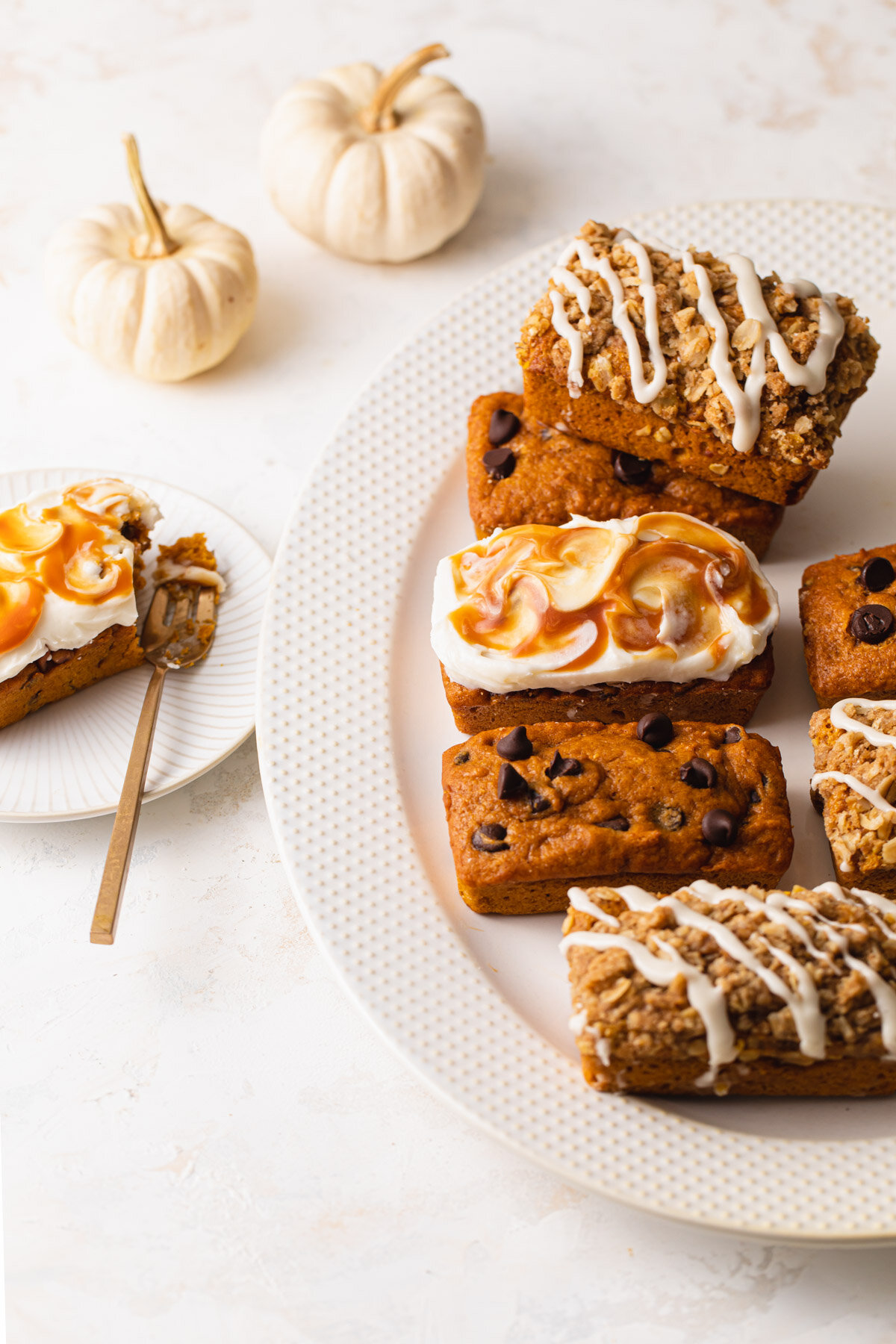 Pumpkin mini loaf cakes on a platter with chocolate chips, vanilla glaze, and caramel cream cheese swirl.
