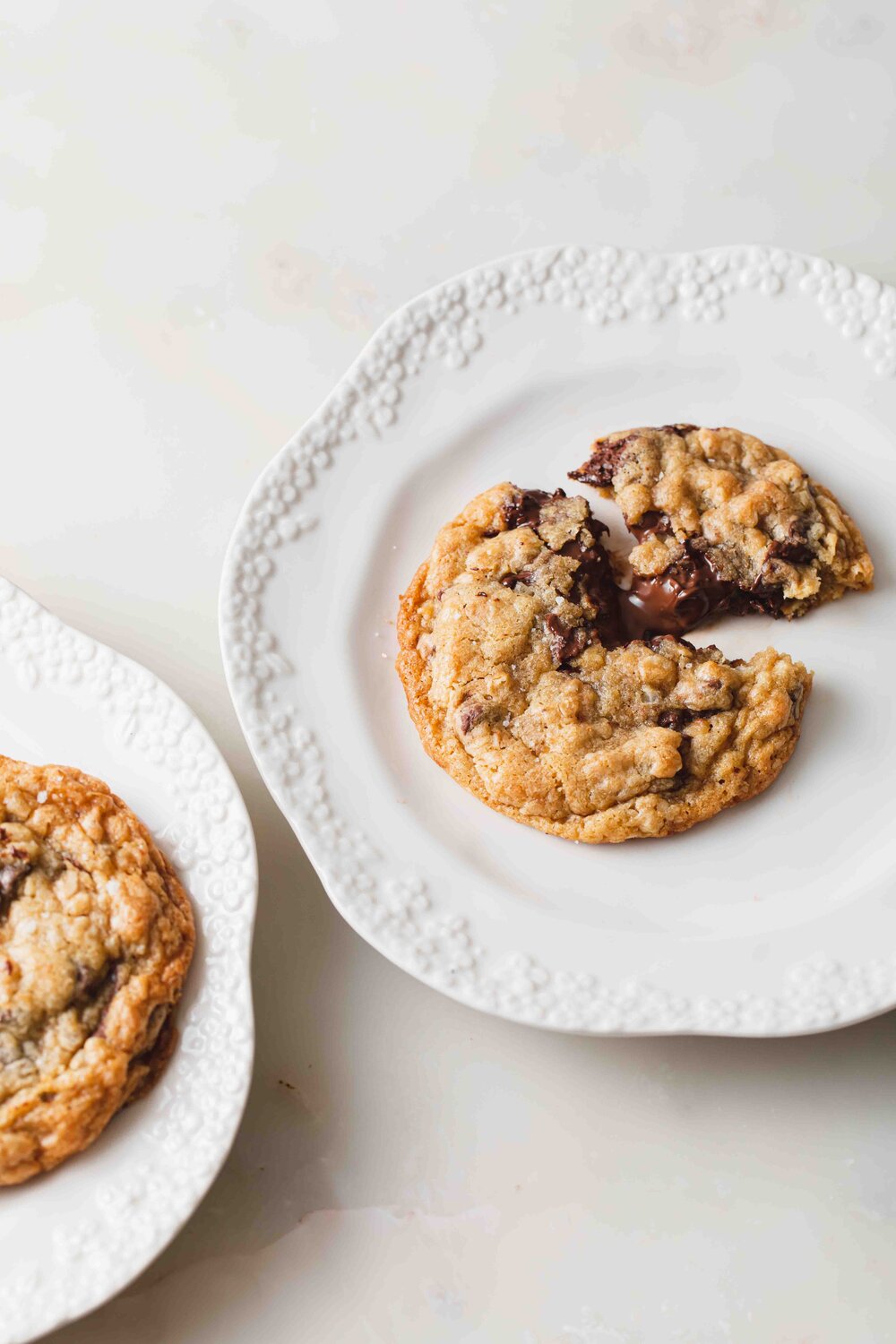 Two plates with Nutella-stuffed Oatmeal Cookies set on a marble tabletop.