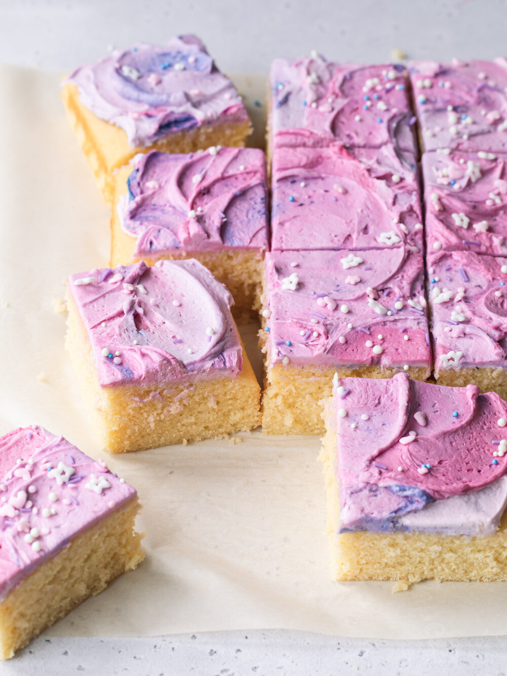 Squares of fluffy vanilla cake with pink and purple whipped buttercream frosting.
