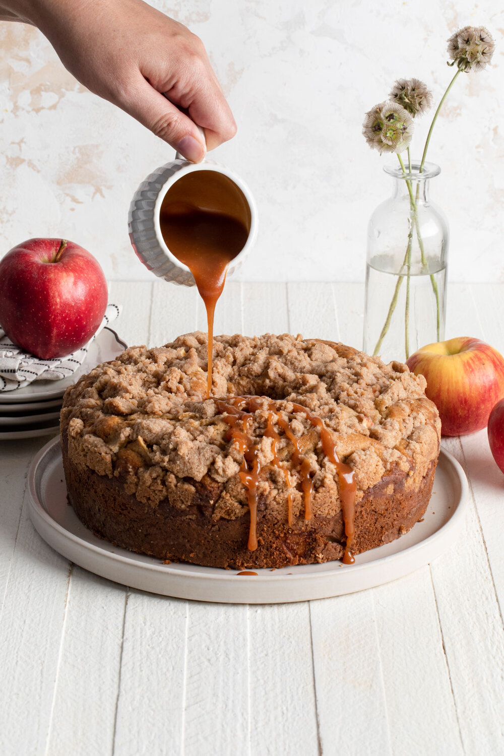 A baked apple coffee cake with caramel sauce being poured over the top.