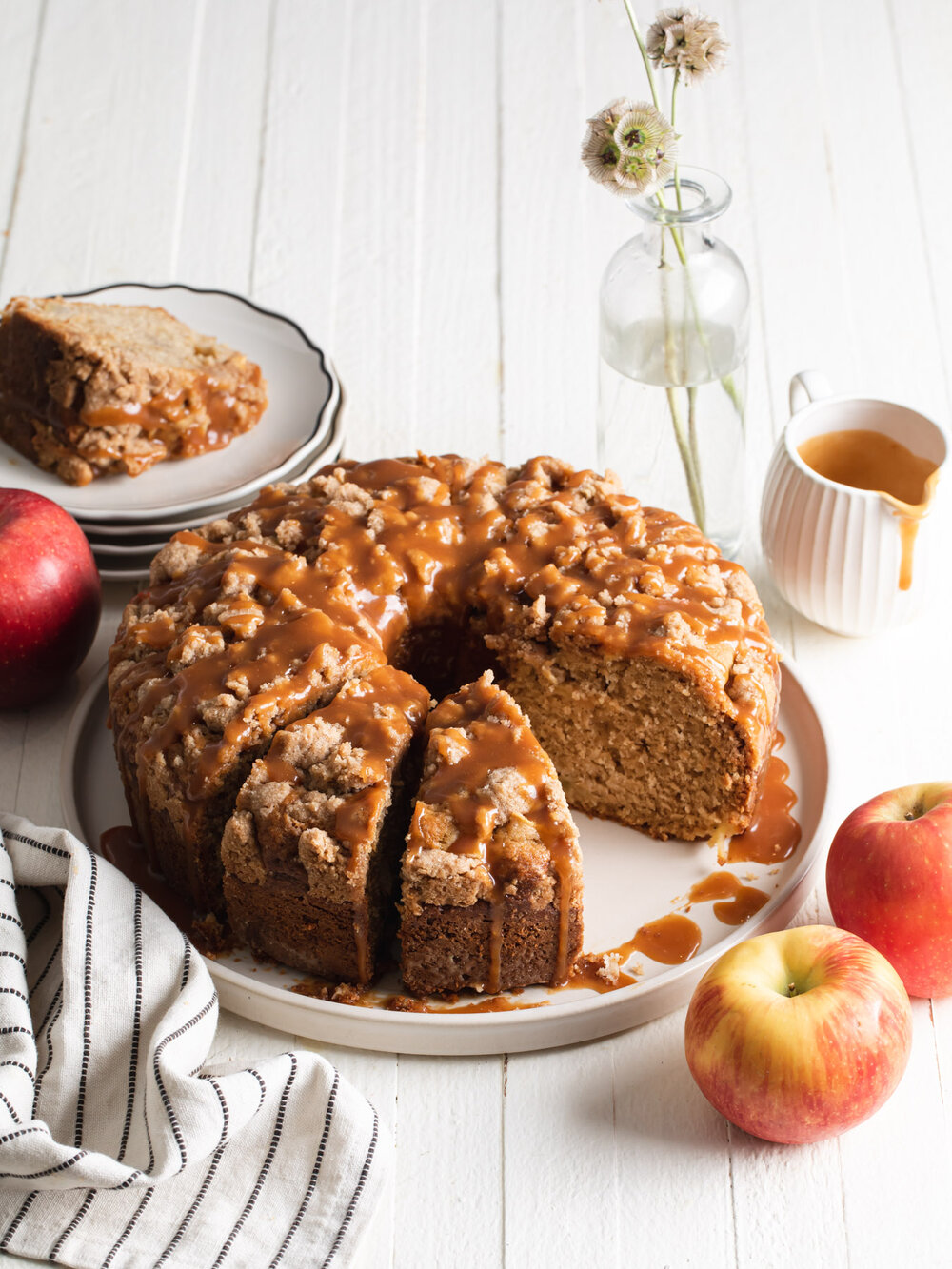 An apple coffee cake baked in a tube-pan and cut into slices with crumb topping and caramel sauce.