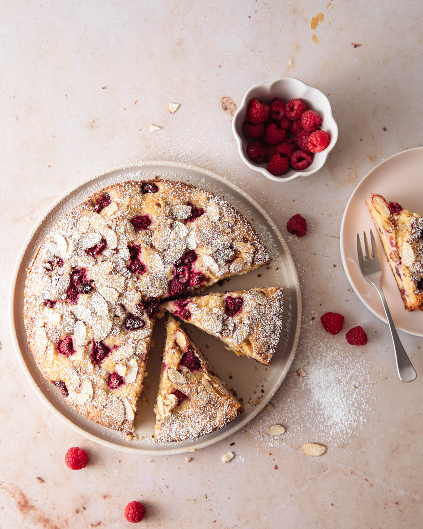 A raspberry almond tea cake with sliced almonds and powdered sugar on top.