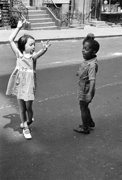 Hashtag Throwback Thursday. Here I am on the east side of Buffalo, New York with my first girlfriend who lived a block away from me on Roebling avenue. I would walk the block to her house, yell her name, and she would come out. We would hold hands until they got sweaty and then we wouldn't. We would play tag. We would dance. This was before I knew anything about Emmett Till, or Trayvon Martin, o r Michael Brown, Jr. This was before I knew about war or death. We were just riding bicycles and smiling. I remember once going back to that old neighborhood on a visit. This was when my mother was still alive. Several years ago. We drove slowly to the neighborhood through deep snow on side streets. We were pointing out houses where our old friends had once lived. She pointed out important houses of her past. They leaned into the wind or were boarded up, their paint peeling. We kind of floated through the neighborhood. I am sure that each of us were remembering lazy summer evenings. The adults sitting on lawn chairs in yards, drinking beer, and playing euchre while their children ran along perfectly clipped lawns shouting. She said, “that empty corner lot there used to be a clam stand. Your father and I used to go on dates there.” Where the clam stand once stood had become an abandoned lot. The lot in the snow became a white square with several scrub trees poking up out of it, but it was beautiful. We drove past the library and the decomissioned church to the main road, which had been plowed. We stopped at the intersection and paused, taking in the scene. The snow and the gloaming had obscured the decay of this forgotten part of the city. It looked like it did when I was young. It looked like it did when everything was easy and carefree and the only problems children had to deal with were the streetlights coming on and taking baths.