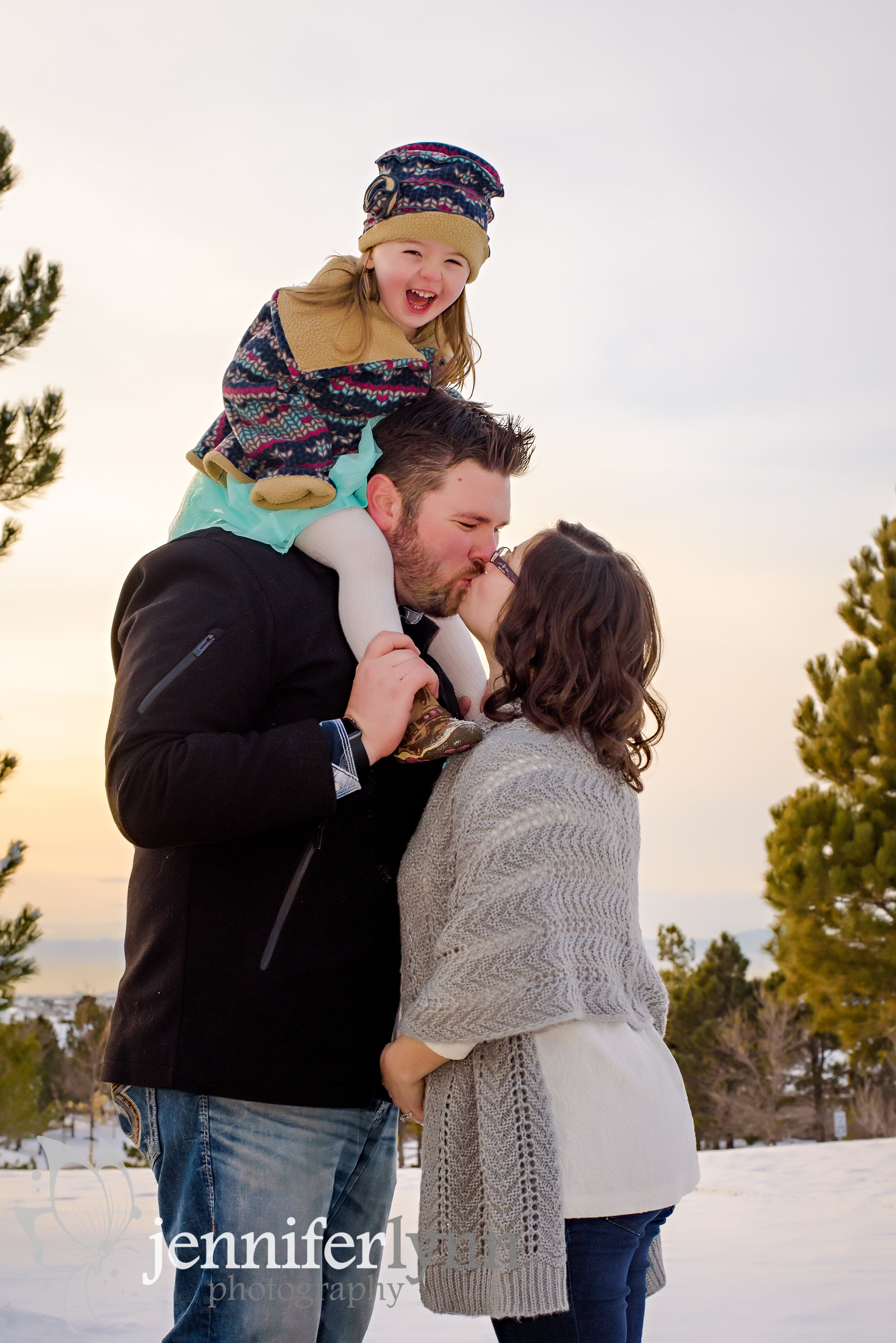 Couple Kissing With Daugher On Dad's Shoulders