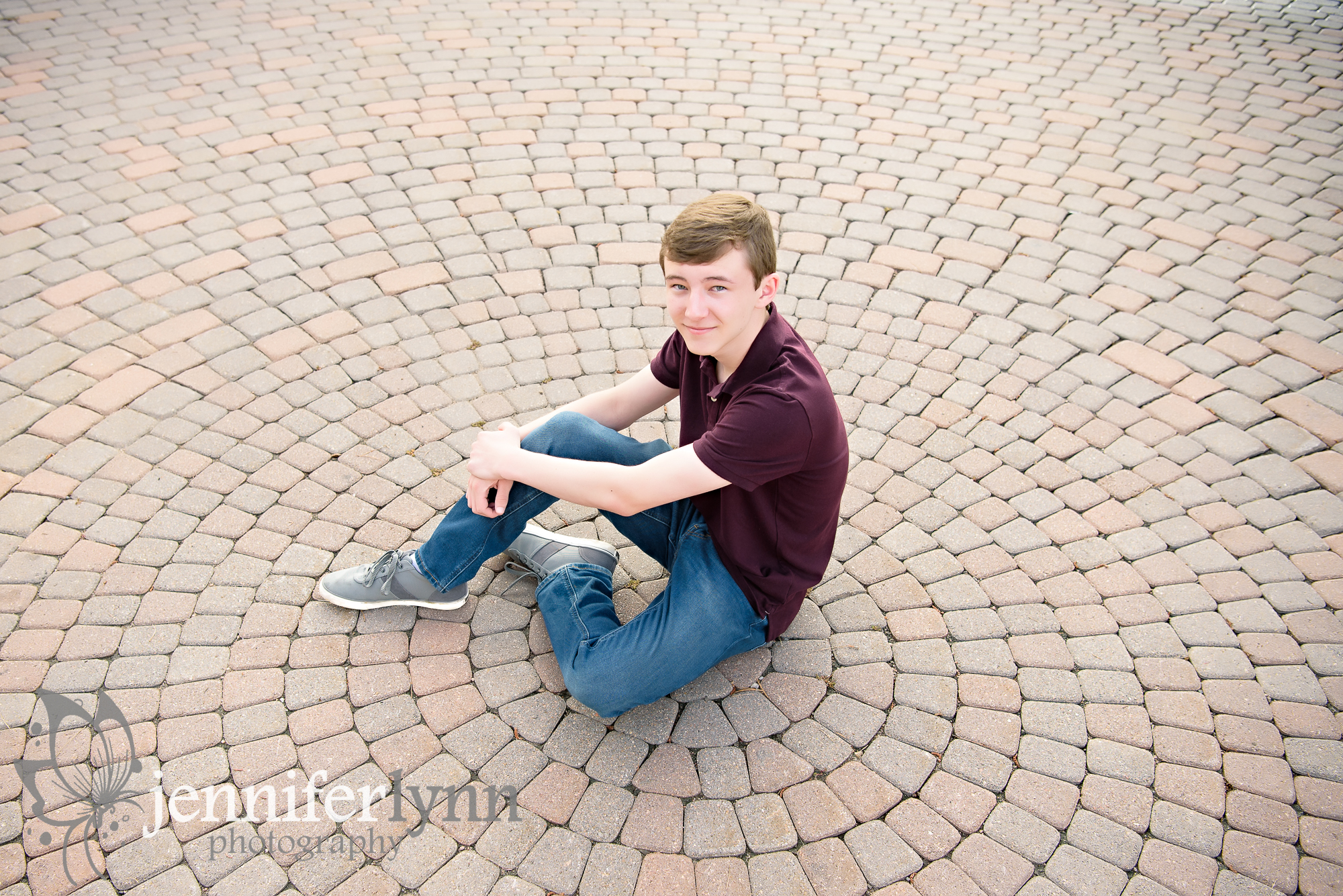 Senior Boy sits on spiral brick patter on ground