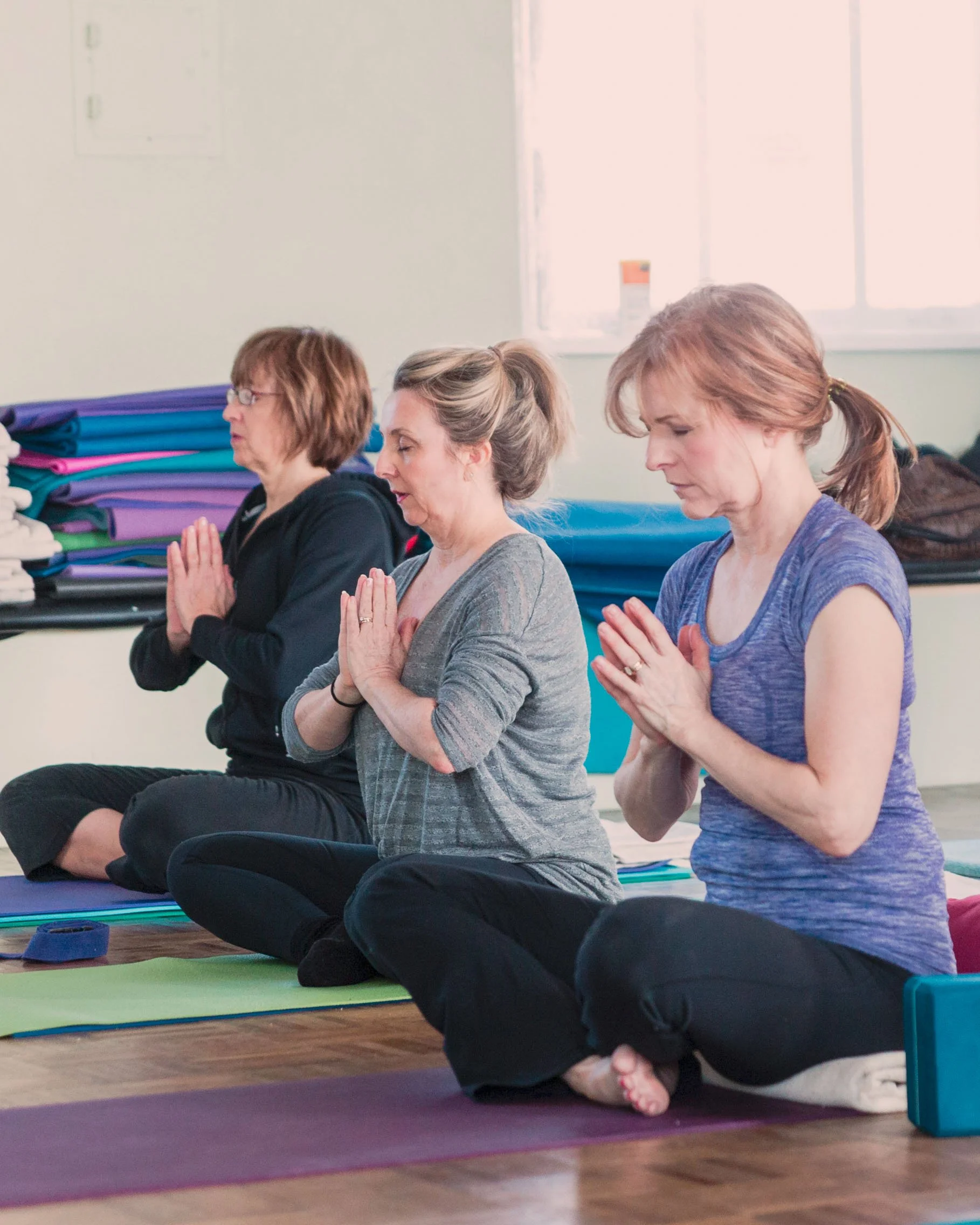 Women seated in a yoga class with hands in prayer, practicing breath awareness and meditation at the downers grove yoga studio