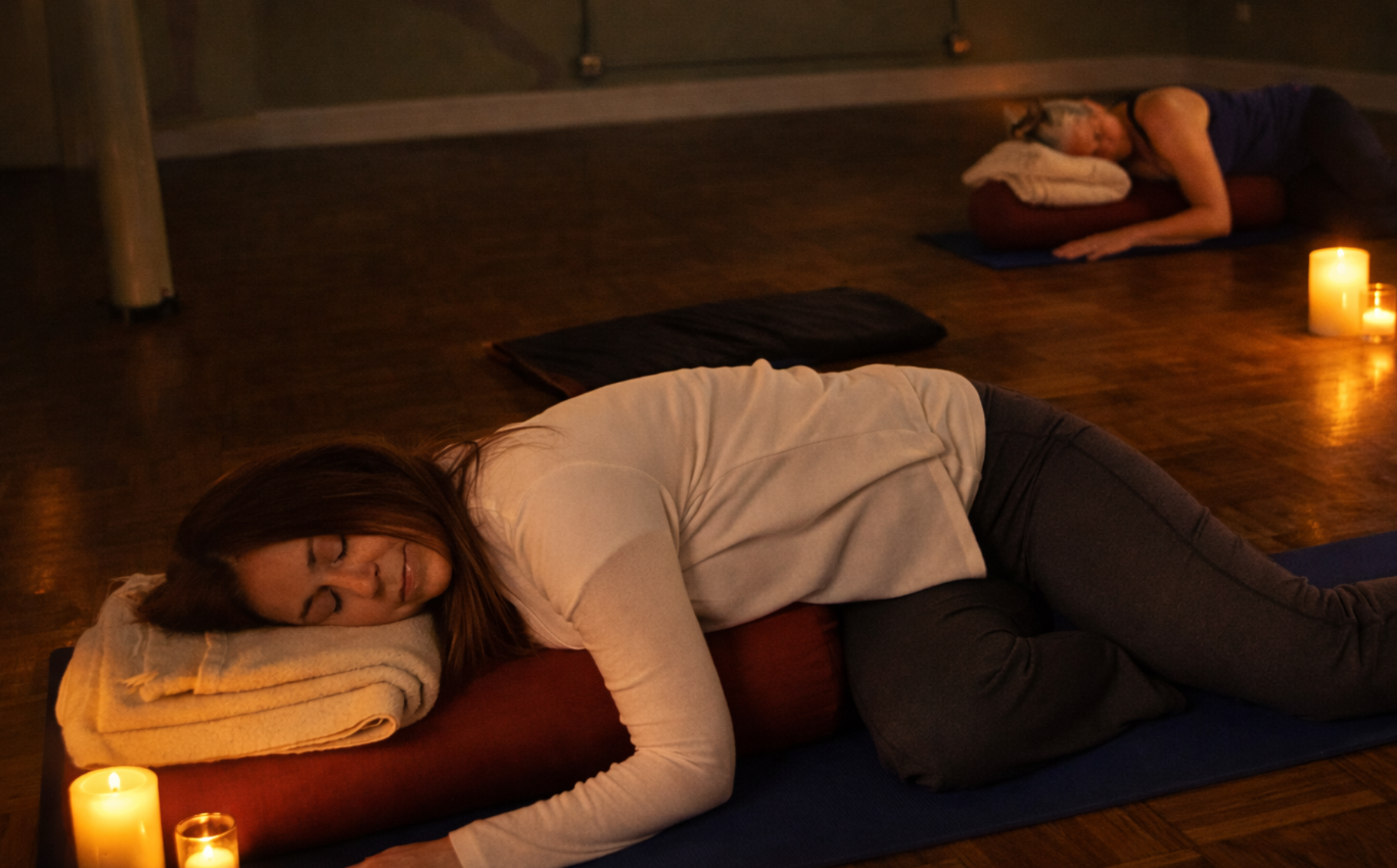 Student resting in supported restorative yoga pose by candlelight during a Yoga Nidra meditation practice at Yoga Among Friends in Downers Grove.