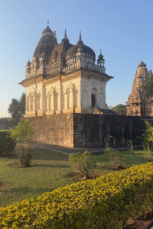 Historic stone temples in India lit by early morning sunlight, surrounded by greenery.
