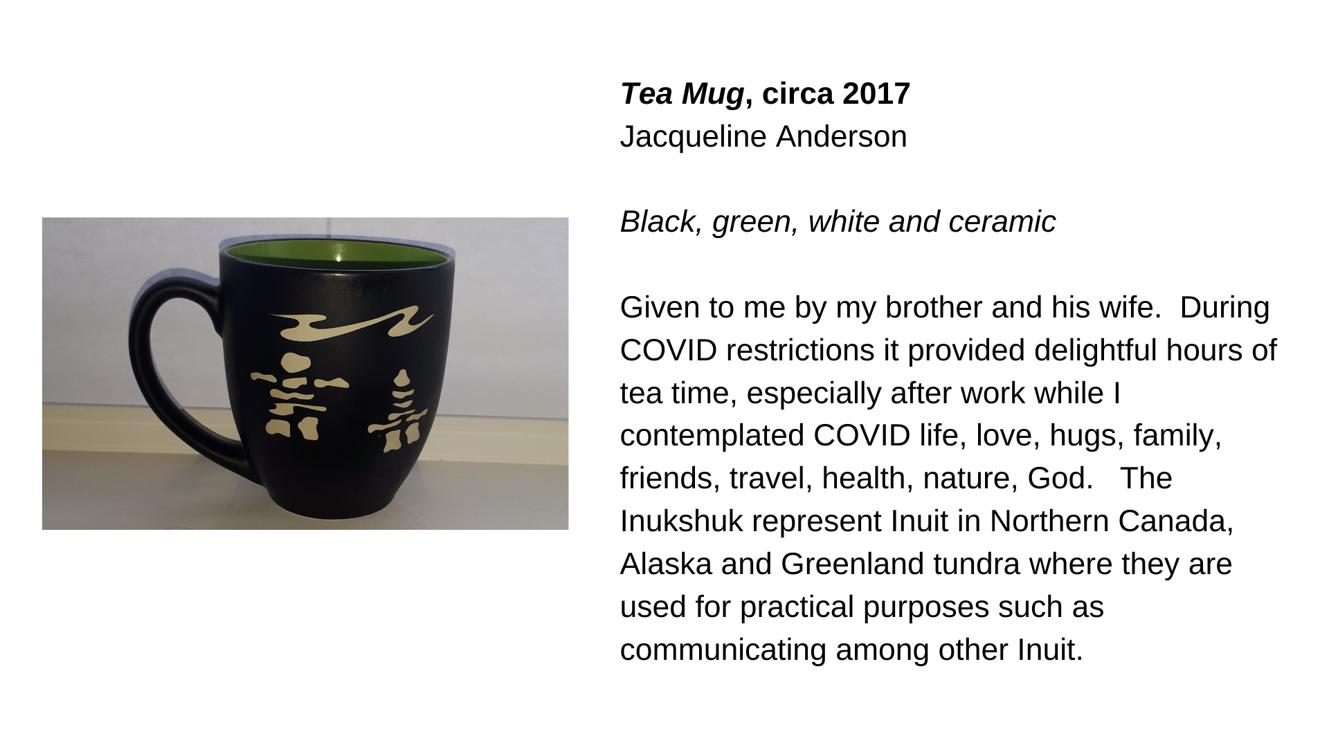  A dark-coloured mug with two inuksuit on it. Next to it is the text, “Tea Mug, circa 2017 - Jacqueline Anderson. Black, green, and white ceramic. Given to me by my brother and his wife.  During COVID restrictions it provided delightful hours of tea 