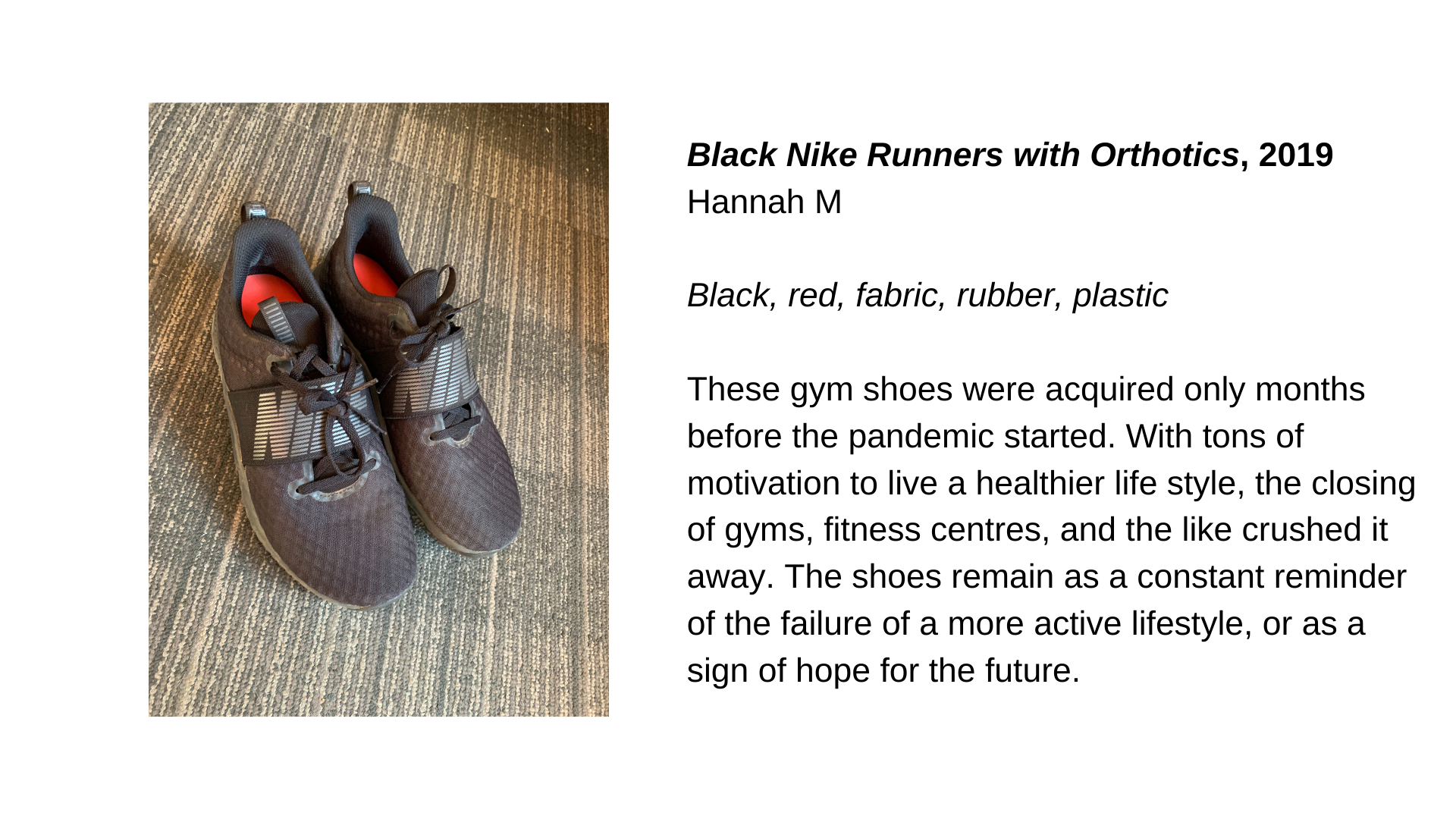  A pair of dark coloured runners with red inserts. Next to this, the text “Black Nike Runners with Orthotics, 2019 - Hannah M. Black, red, fabric, rubber, plastic. These gym shoes were acquired only months before the pandemic started. With tons of mo