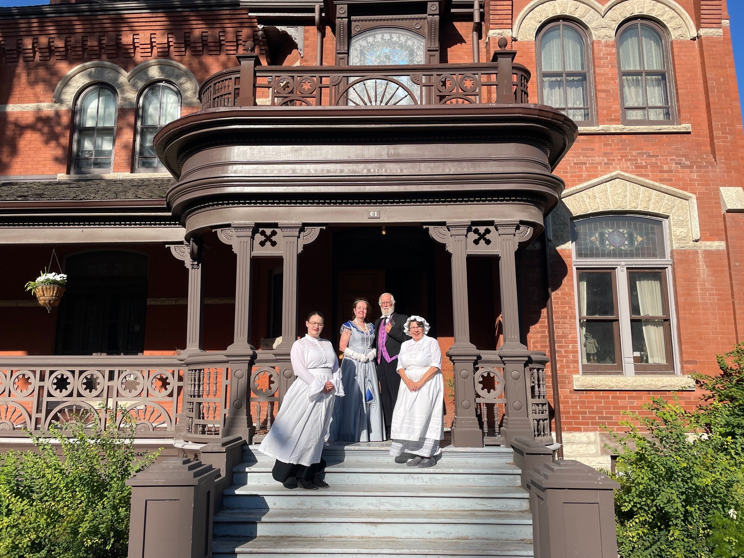  Four volunteers stand on the front steps of Dalnavert in historical clothing 