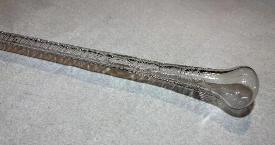 a close up of a clear blown glass witching wand, in the shape of a staff. The glass was twisted while being blown, creating an intricate spun pattern.