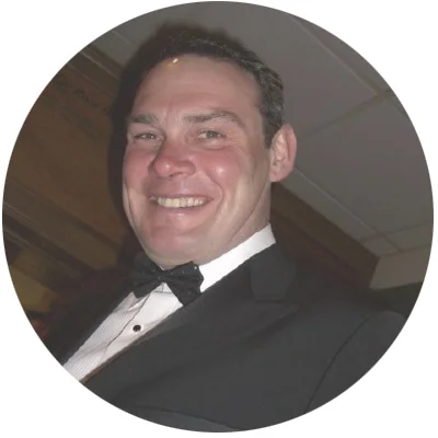 A smiling man in a tuxedo with a bow tie, at an indoor event.