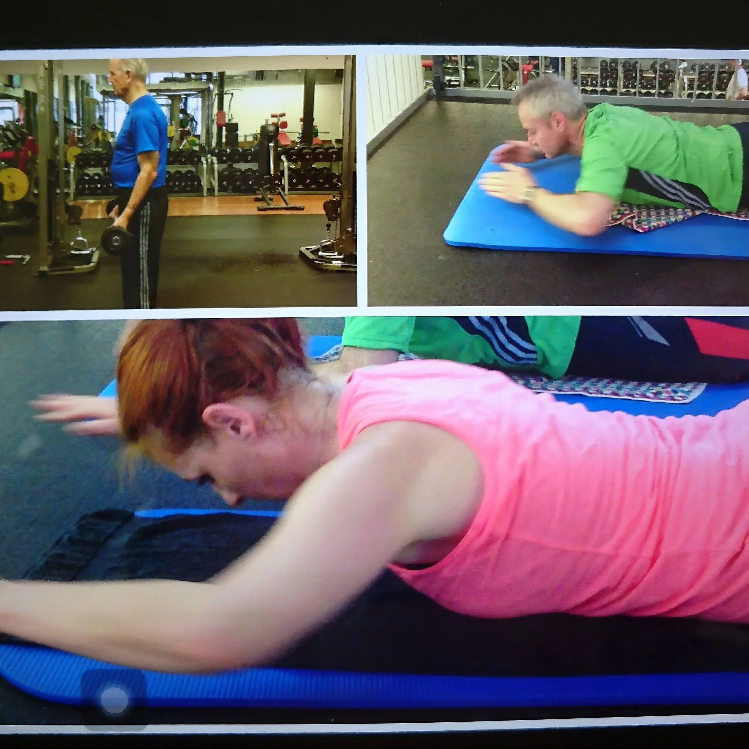 Three people exercising in a gym: an elderly man lifting dumbbells, a man doing a forearm plank on a blue mat, and a woman stretching on a blue mat.