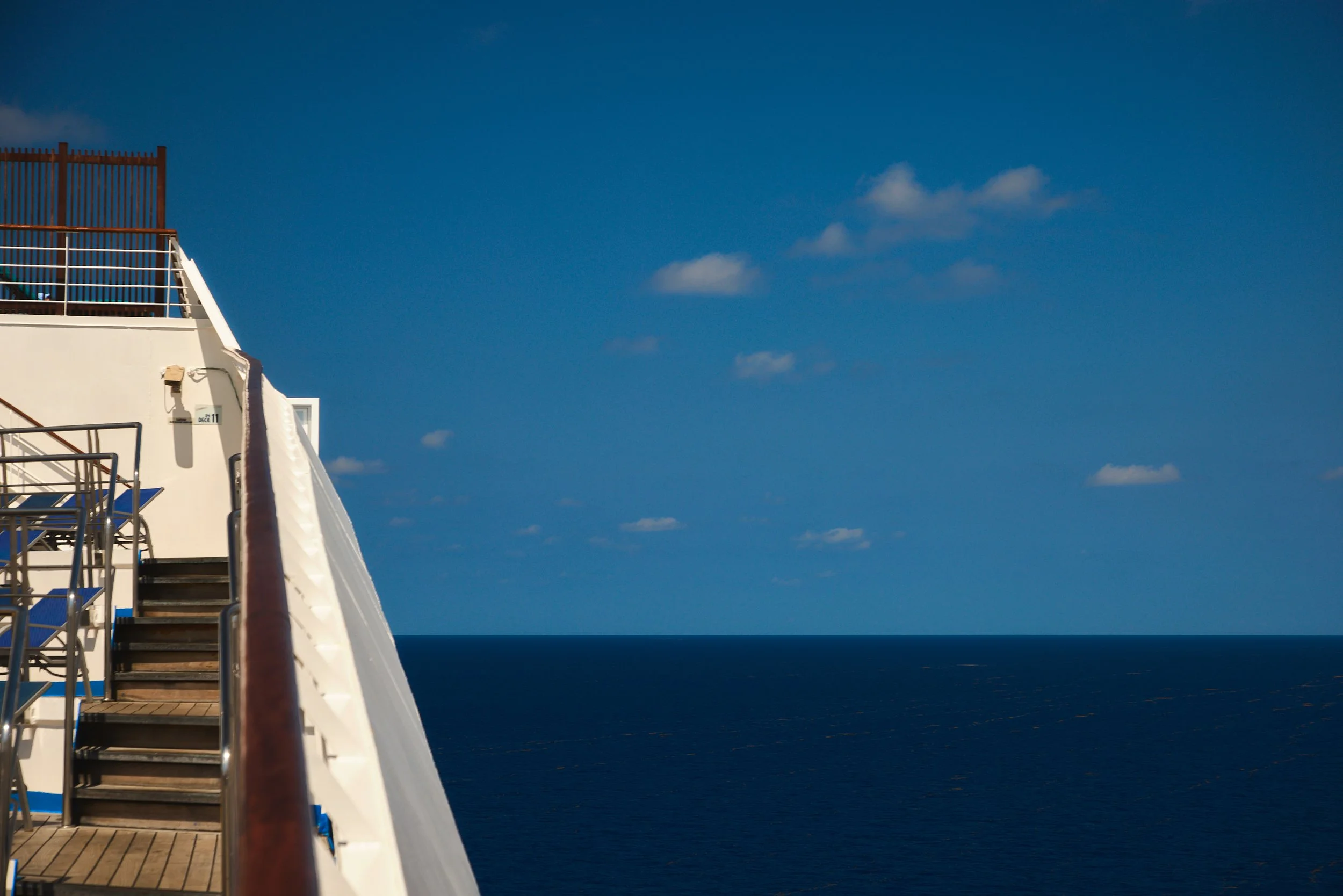 View of the ocean with a white building structure featuring metal stairs and railings on the left, under a clear blue sky with a few small clouds.
