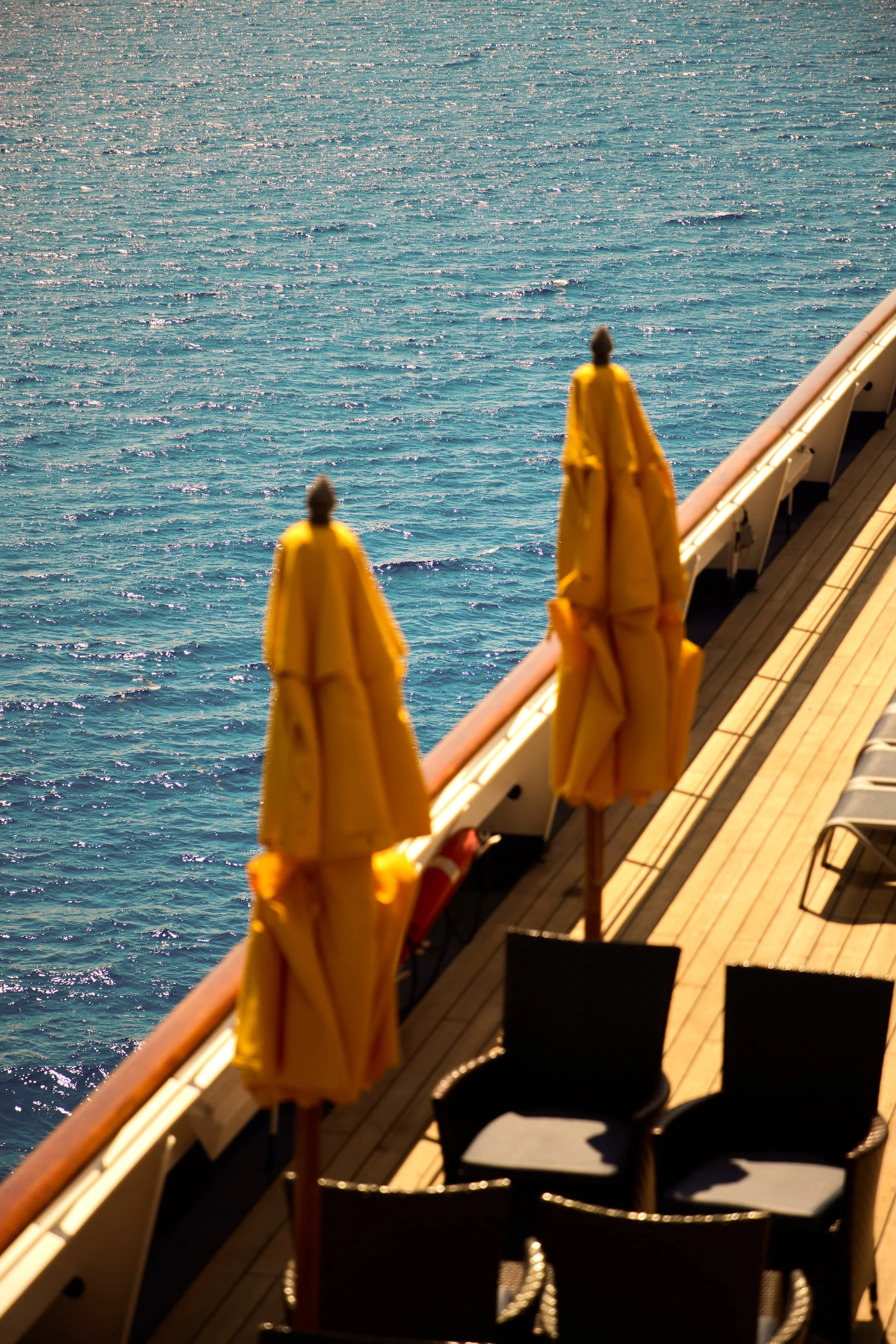 Several yellow umbrellas on the deck of a cruise ship with a view of shimmering blue ocean water.