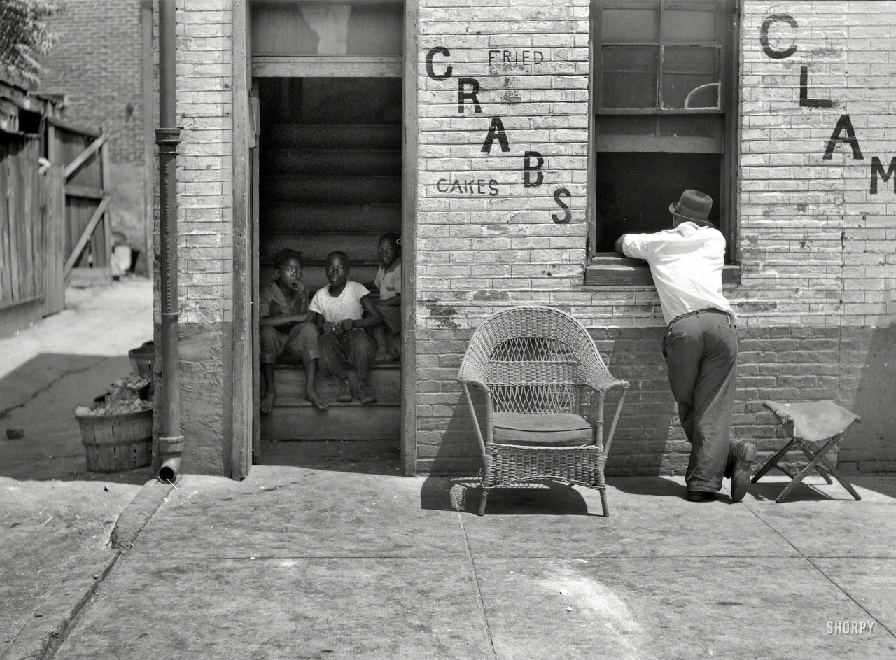 “House in Negro section of Baltimore, Maryland." July 1938. Medium-format nitrate negative by John Vachon. For a larger version: http://bit.ly/1sqTn73
After a sweaty-palmed trip over the long Chesapeake Bay Bridge, many beachgoers make habitual yearly stops on their annual exodus to Ocean City at many of the crab houses on Kent Island. But they weren’t always massive waterfront establishments with gorgeous views of loblolly islands and watermen coming and going. As this photo reminds us, the original "crab houses” would have been the kitchen in a private home, where a local lady made some extra cash by cooking up and serving crabs to her hungry neighbors. In the sweltering belly of a Baltimore summer, the smell of a proprietary blend of spices would have clouded in the humidity, a savory London fog and invisible shop sign. Crabs, clams, fried or cakes wrapped in newspaper, all to be carried off and eaten on a quiet stoop with salty fingers and a glowing, greasy chin.