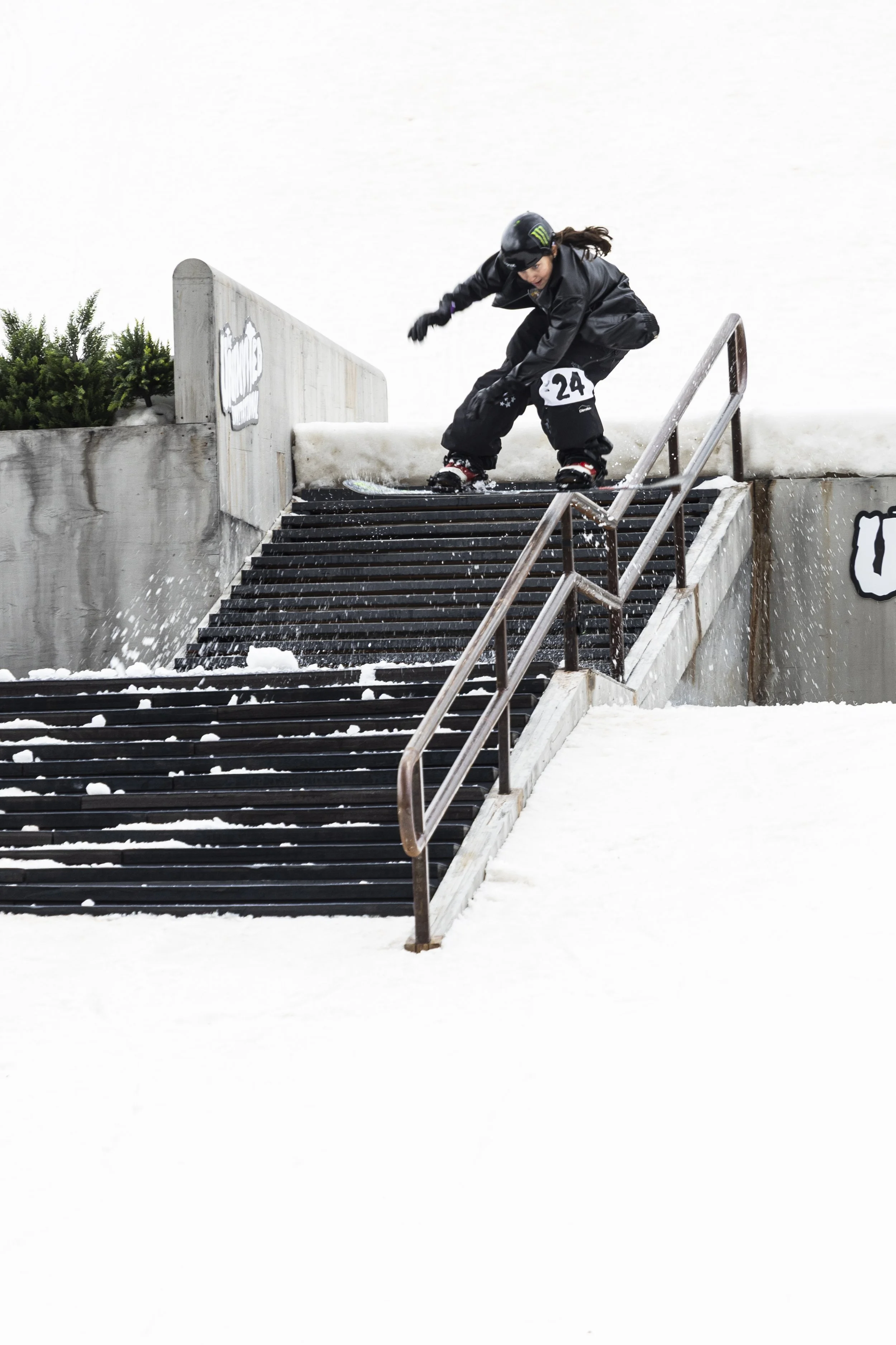 A person in black clothing, helmet, and ski gear falling or sliding down metal stairs covered in snow at a ski resort.