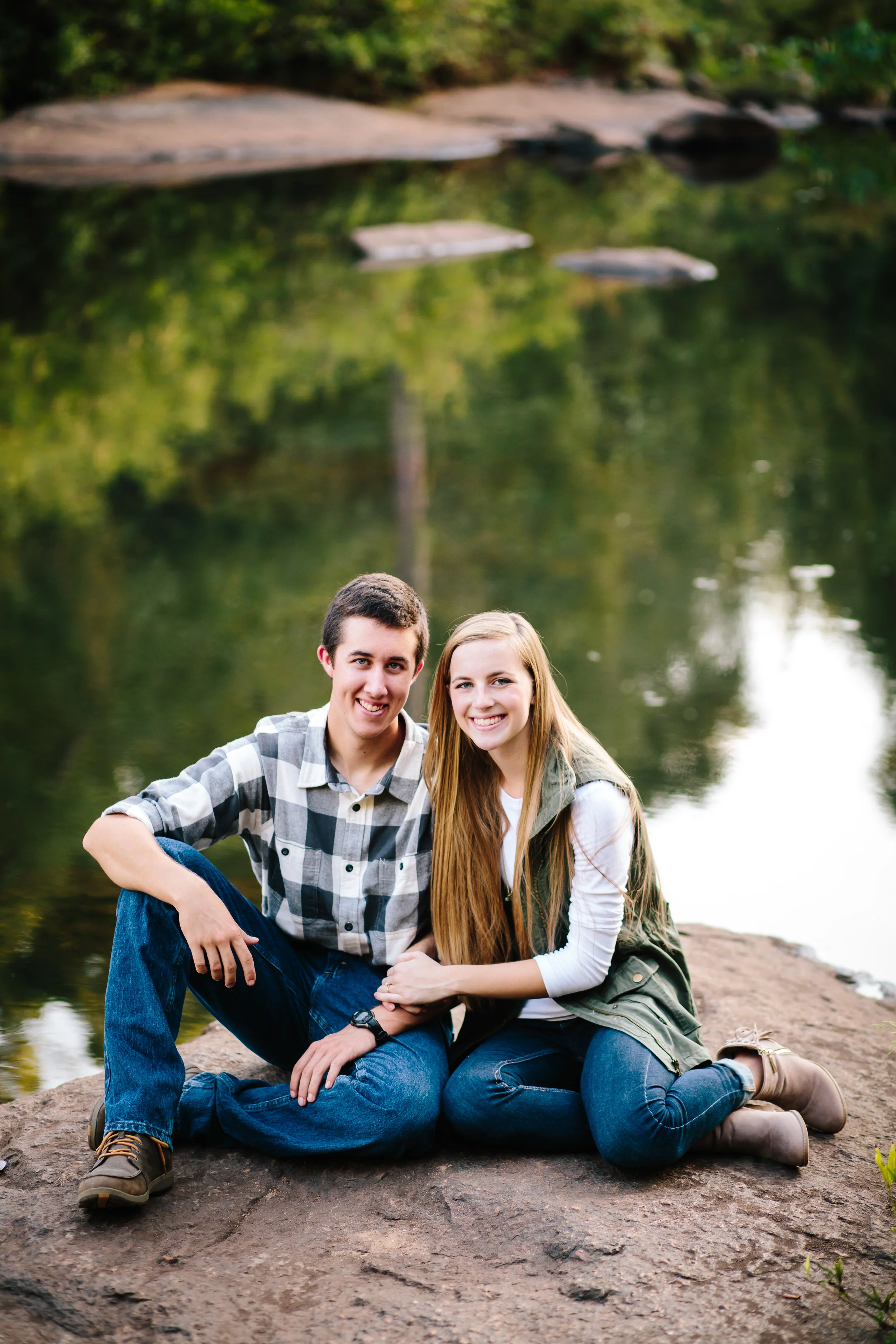 Young Couple Sits on Rock By Water - Engagement Photography
