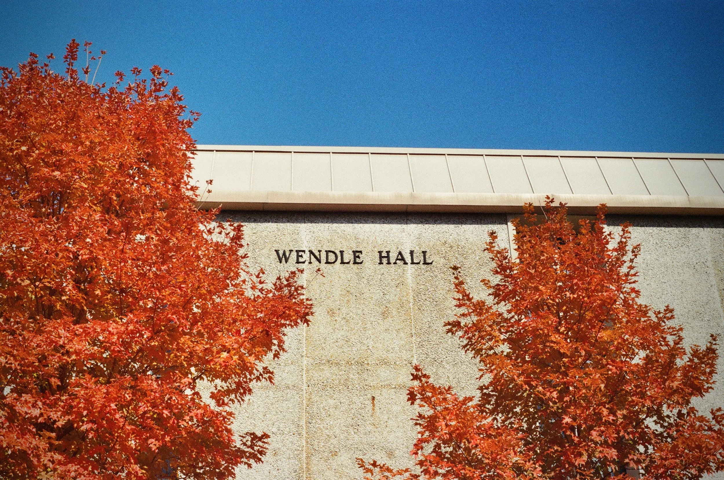 Side of a modernist campus building with the words Wendle Hall on the site. Trees w/ orange leaves in the foreground.