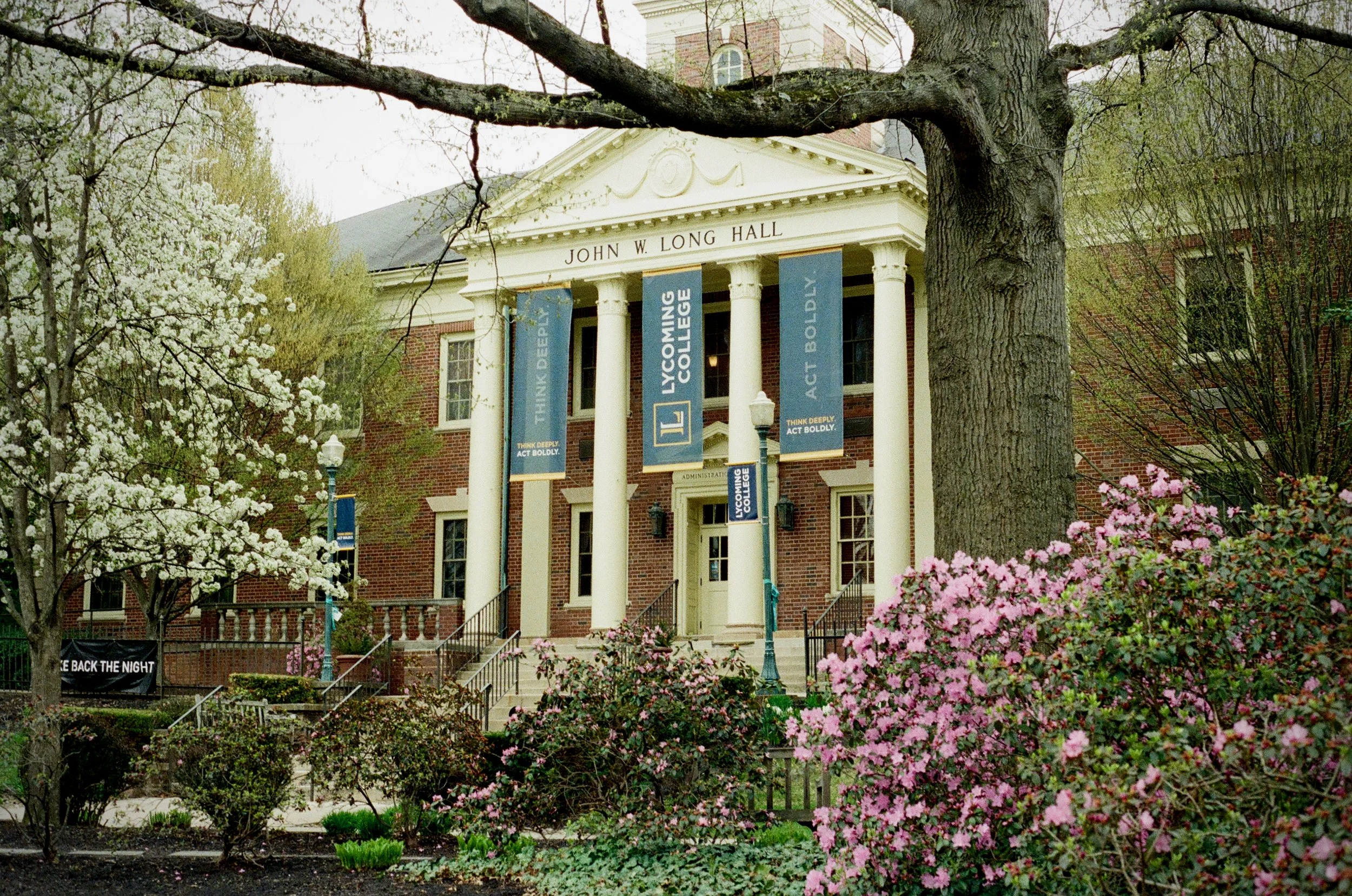 Campus administration building with blossoming trees and bushes in front of it.
