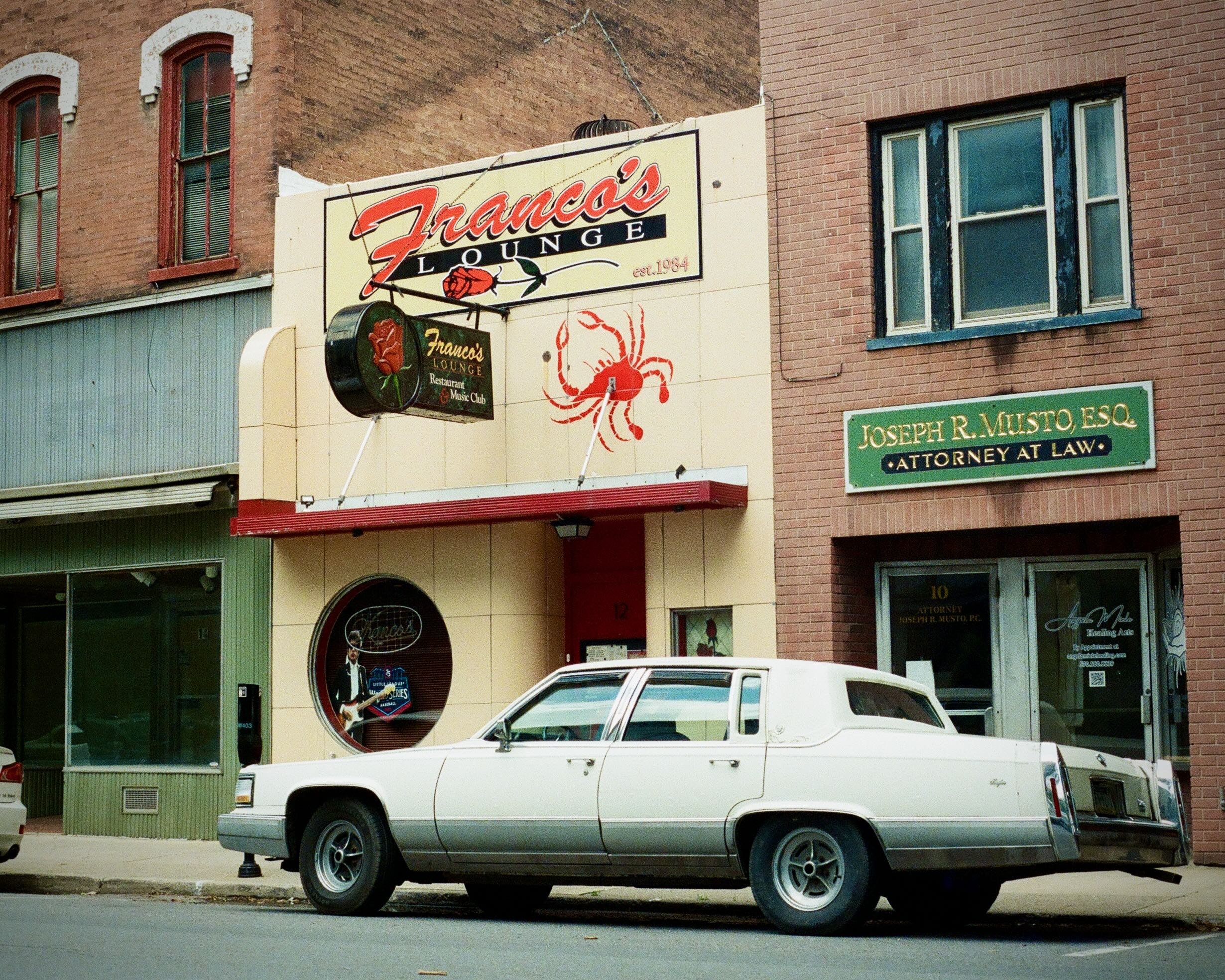 Cadillac parked on a city street in front of a lounge.