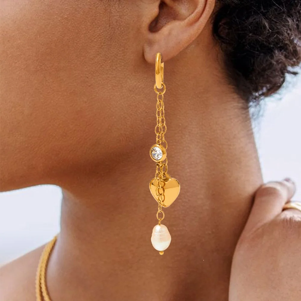 Woman wearing 18k gold plated dangle earrings with heart and pearl charms.