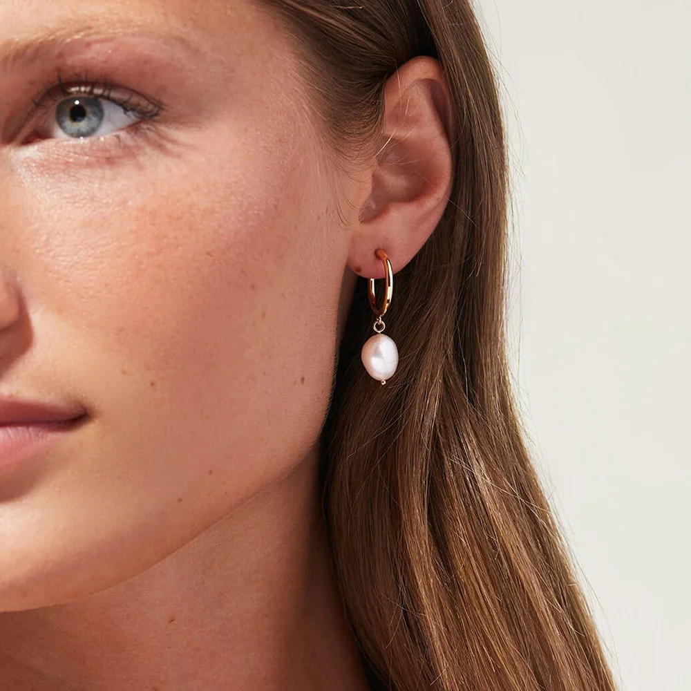 Woman wearing gold freshwater pearl hoop earrings.