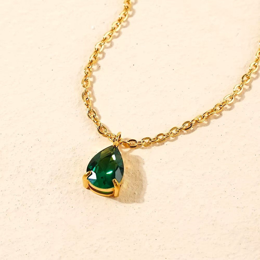 A gold chain with a teardrop shaped emerald green gemstone pendant.