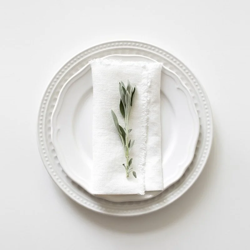 White fringe cotton linen dinner napkins on table setting.