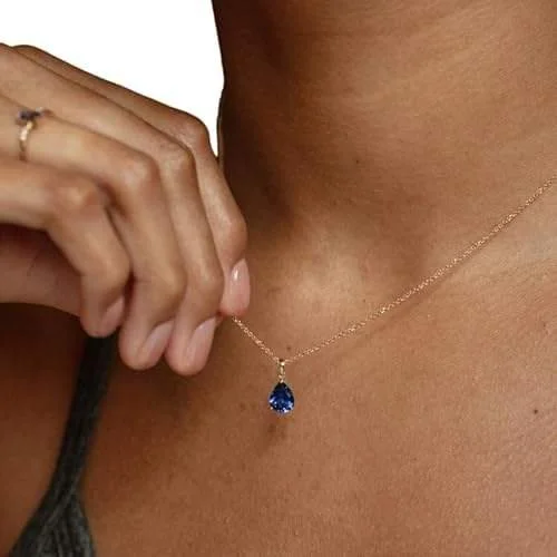 Woman wearing a blue sapphire pendant necklace with an adjustable clasp closure.