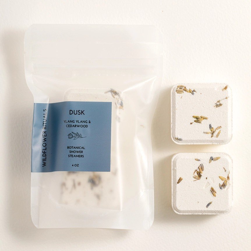 Two ylang ylang scented botanical shower steamers packaged in an eco-friendly bag.