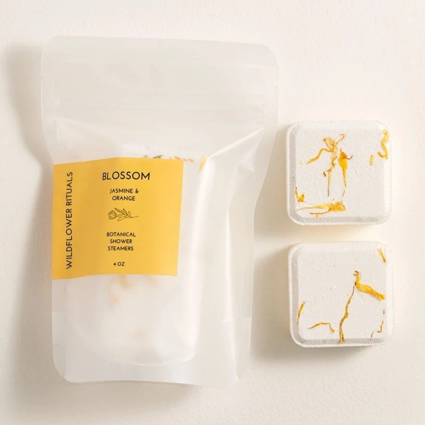 Two jasmine and orange scented botanical shower steamers packaged in an eco-friendly bag.