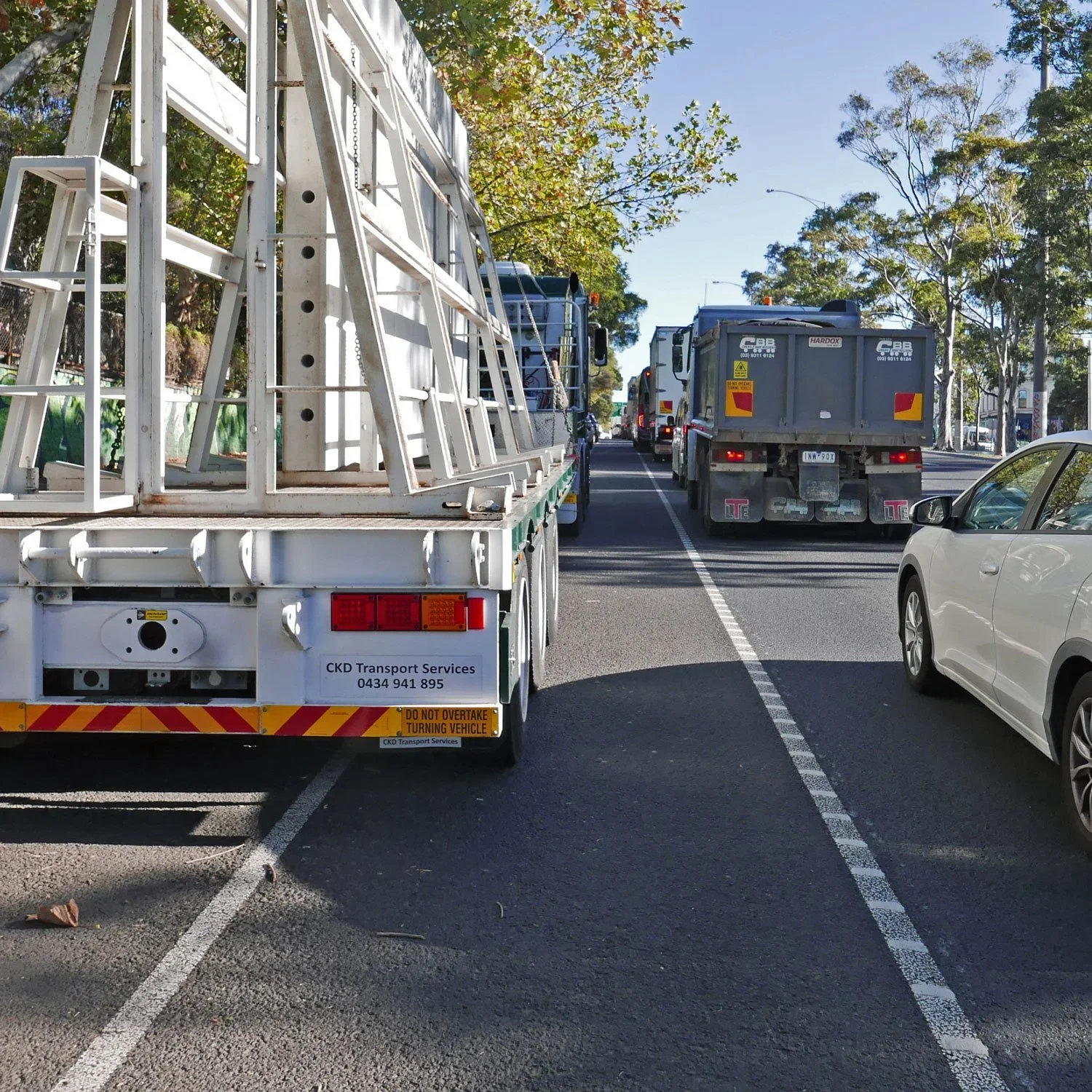 A painted bike lane with large trucks on either side.  The parked truck on the left has its wheels well out into the bike lane.