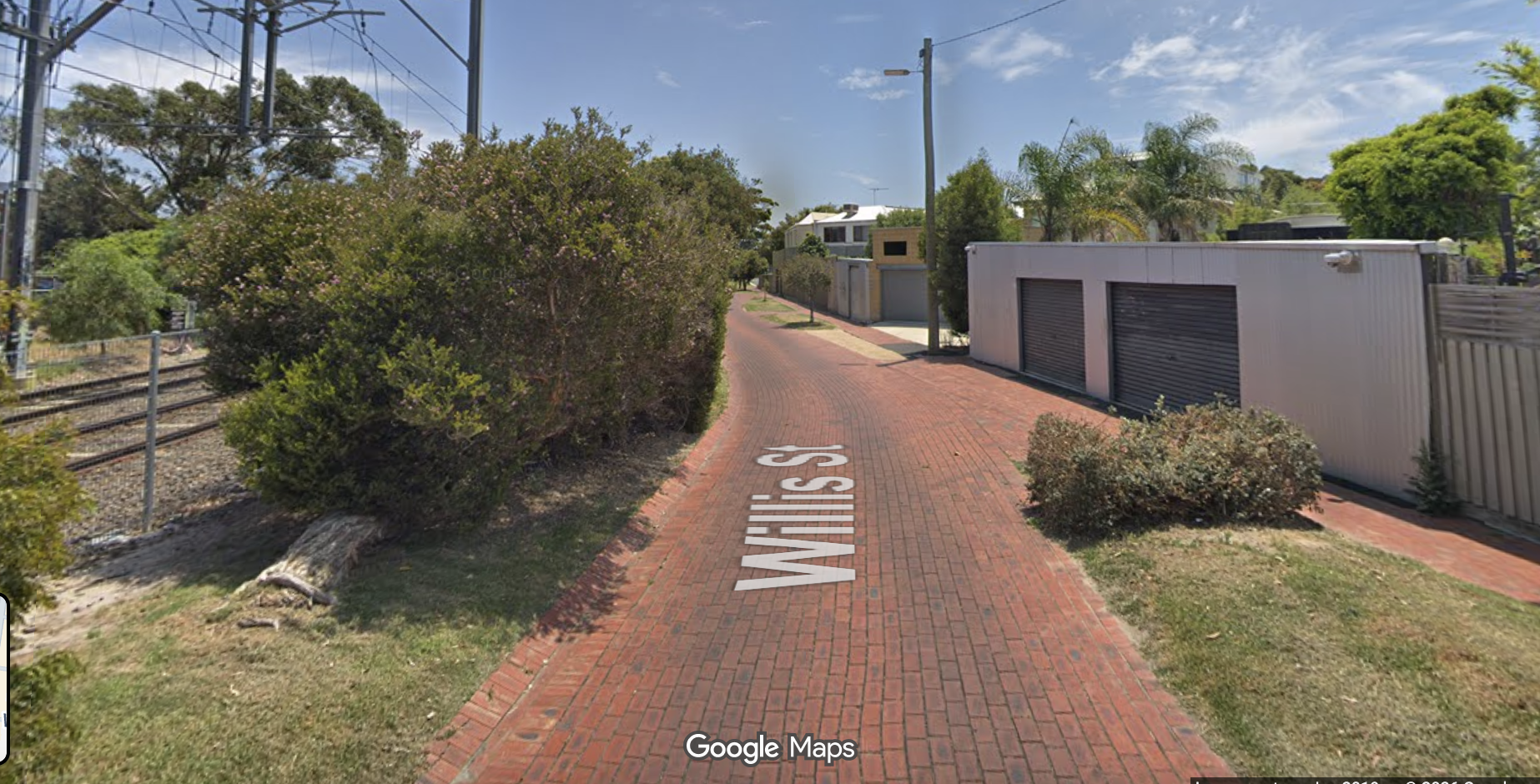 A narrow street with brick surface, with shrubs to the sides