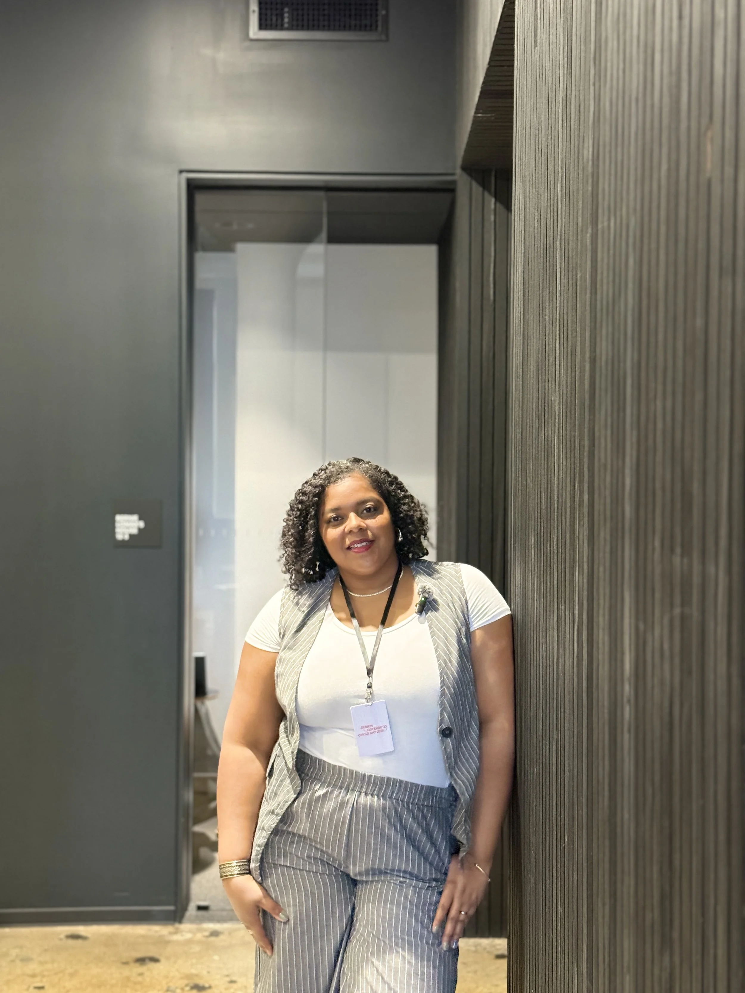 A woman with curly hair, wearing a pinstripe vest and matching pants, and a white top. Small Business educator on branding and marketing.