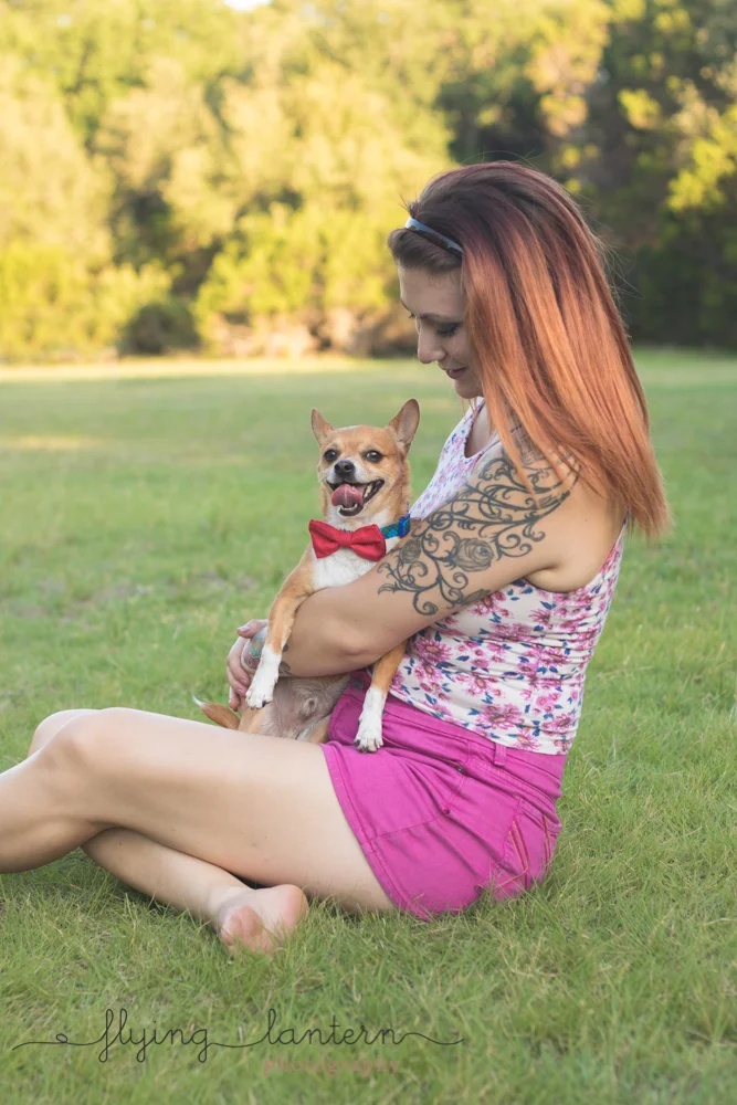 owner sitting in grass holding dog looking down