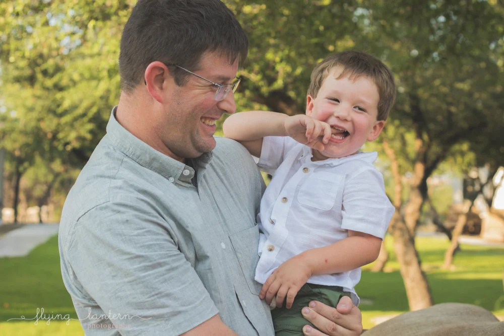 son held by dad and sticking finger in mouth