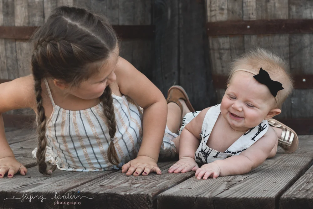 older sister and baby sister looking at each other and giggling