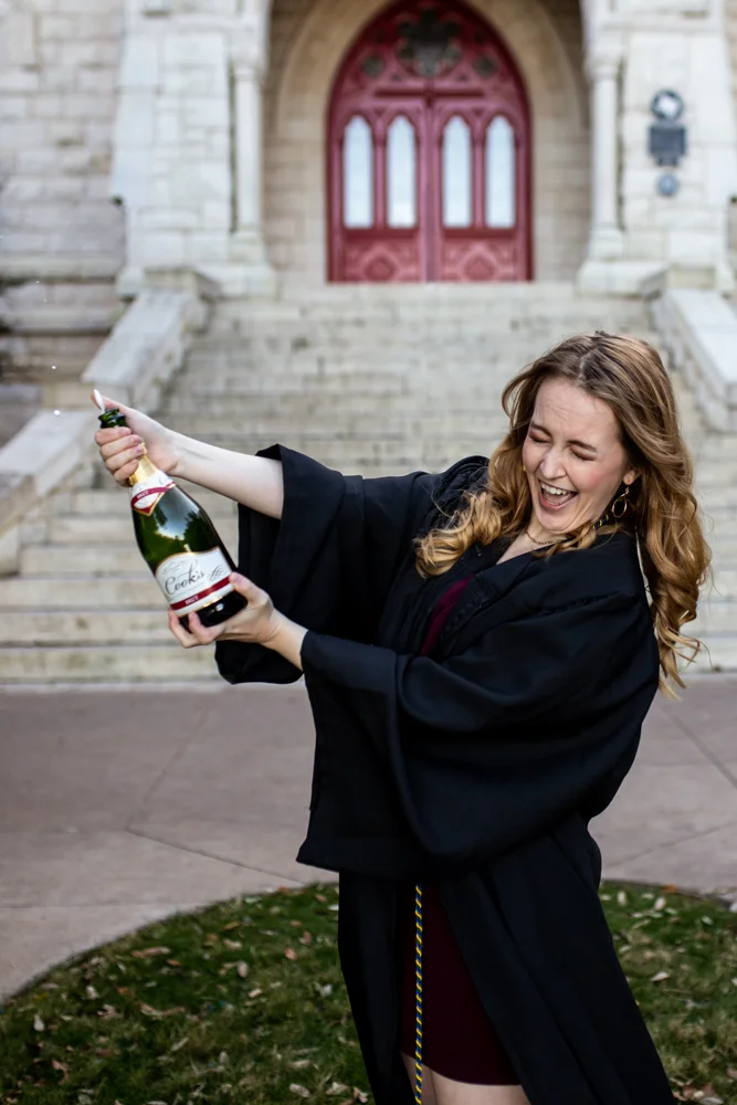 Senior portrait of girl at St. Edward’s University in front of main building popping champagne bottle. Photo by Erin Reas Austin, TX photographer