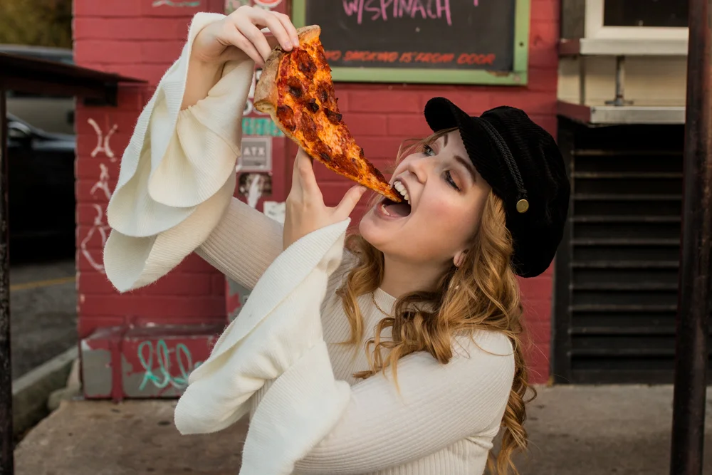 Girl senior portrait outside Homeslice eating a slice of pepperoni pizza. Photo by Erin Reas photographer in Austin, TX