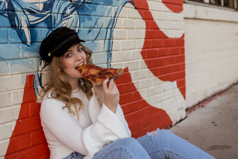 Girl senior portrait outside Homeslice eating a slice of pepperoni pizza. Photo by Erin Reas photographer in Austin, TX