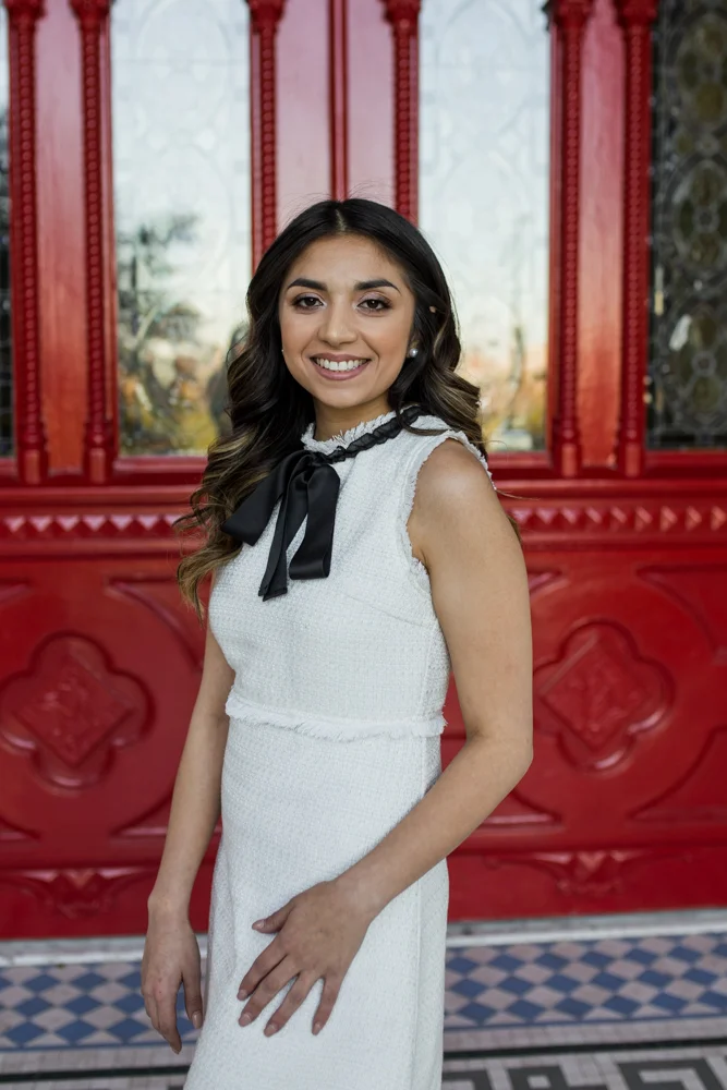 female college graduate standing in front of red doors at st. edward’s university