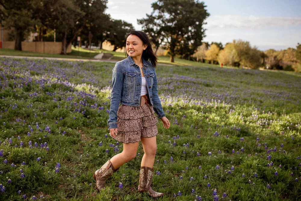 Female lifestyle portrait walking through bluebonnet field at St. Edward’s University. Photo by Erin Reas senior photographer in Austin, Texas.